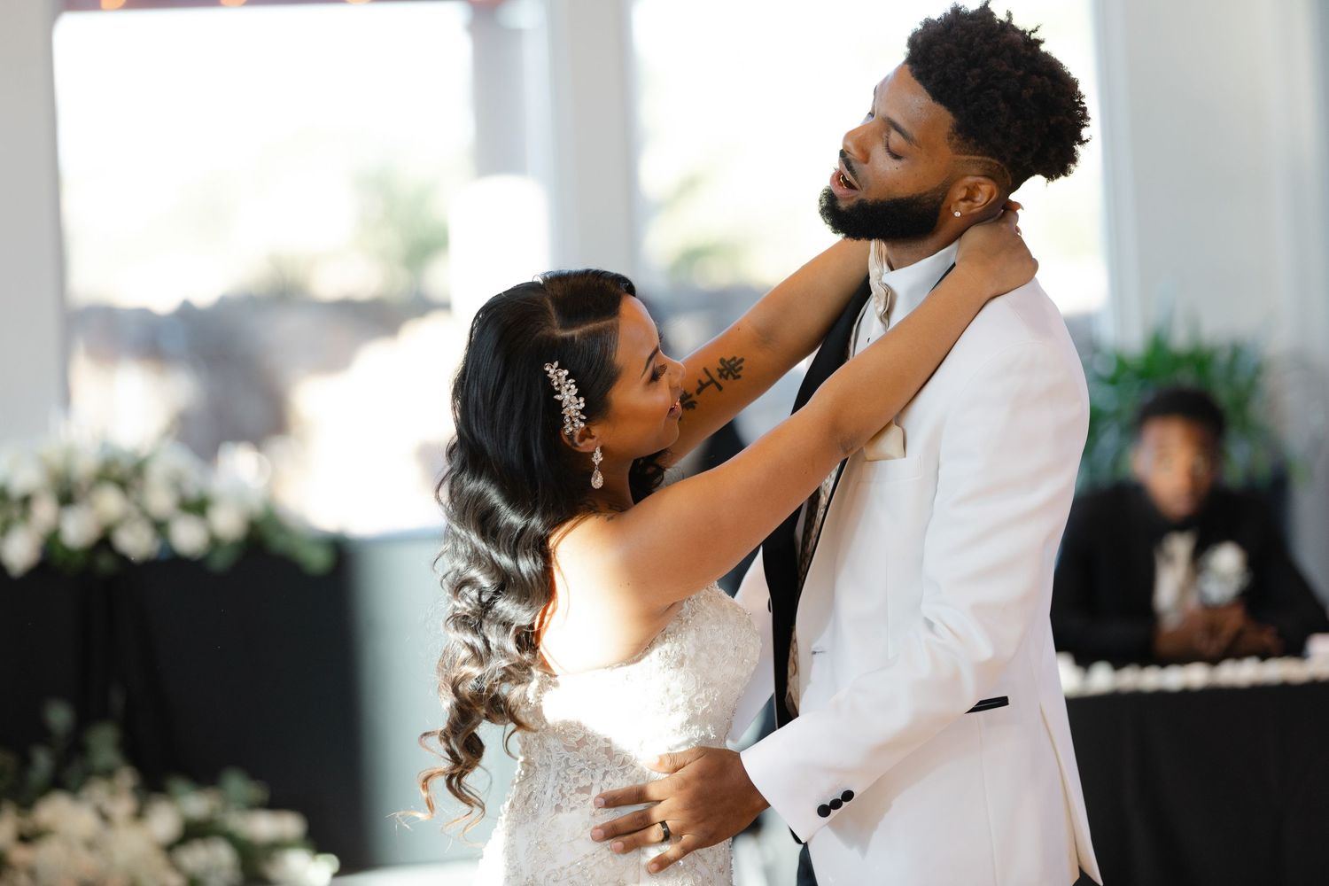 Romantic first dance moments between newlyweds in a light-filled reception space with white decor.