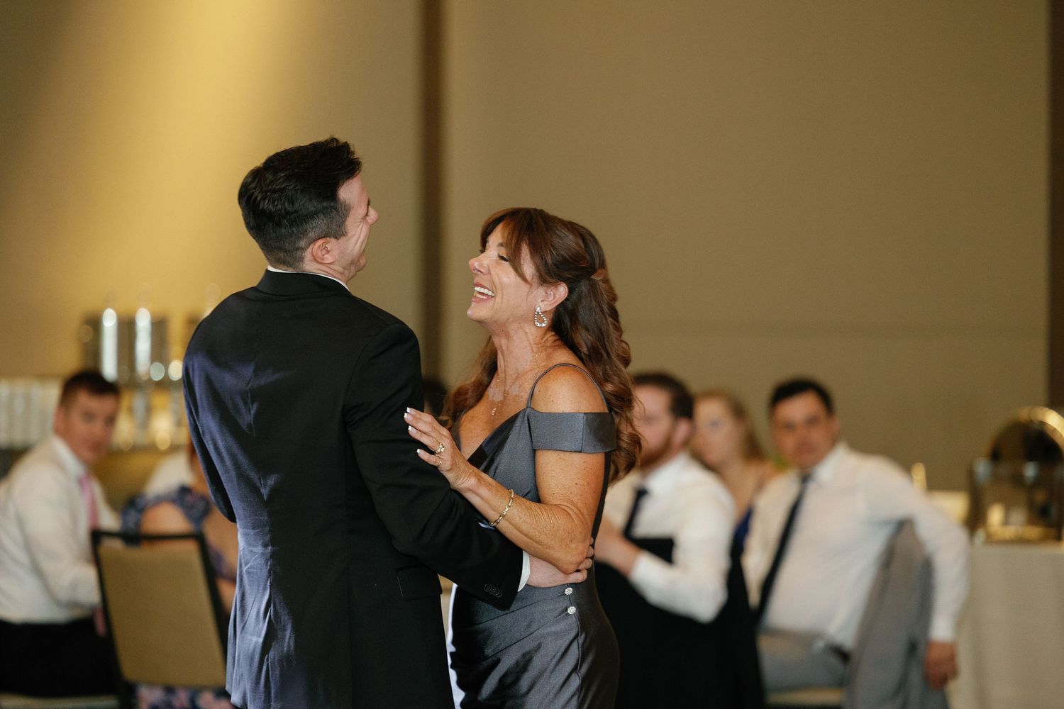 A couple shares a romantic dance together at a formal event while guests look on in the background.