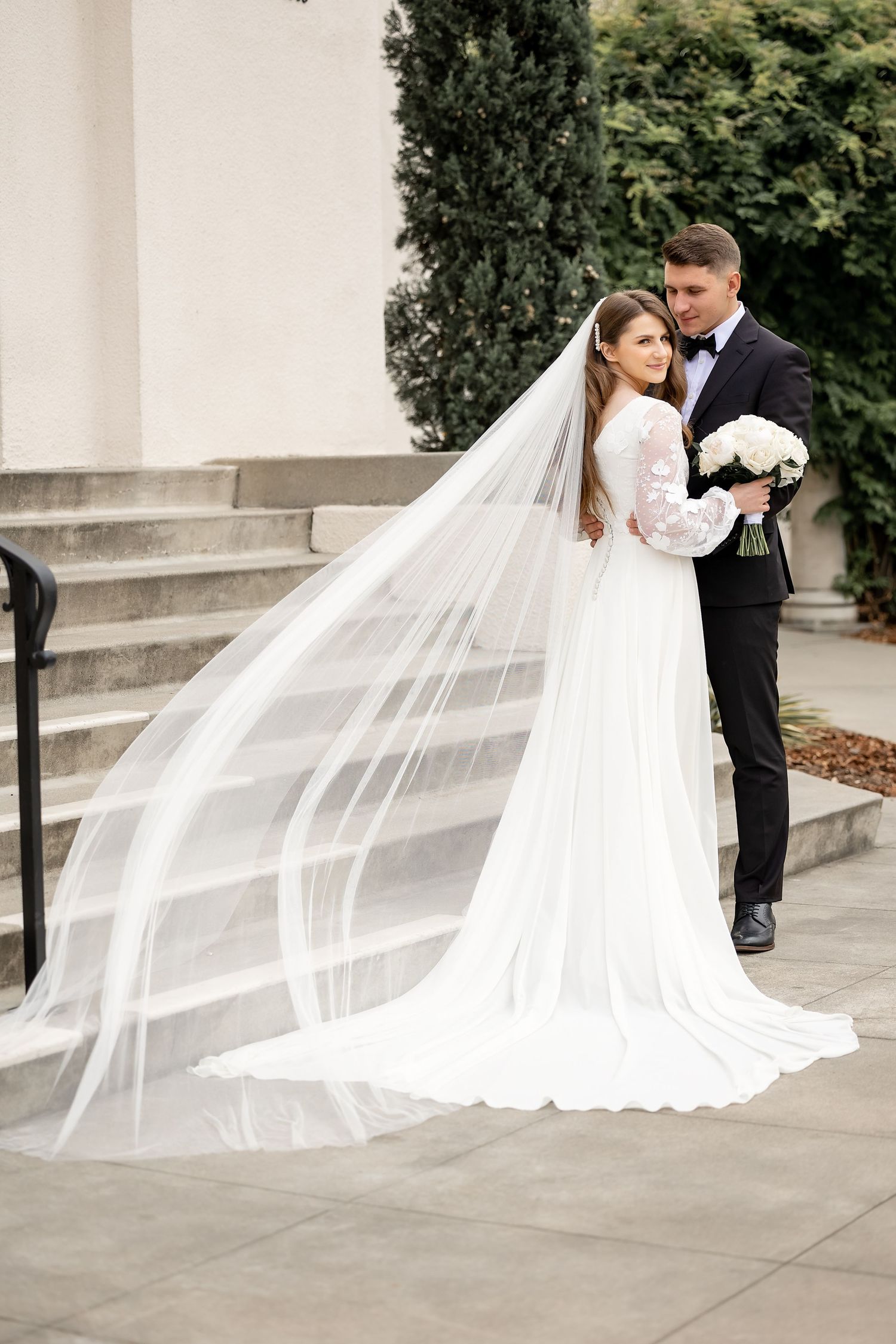 Wedding couple poses on concrete steps with flowing veil creating dramatic composition.