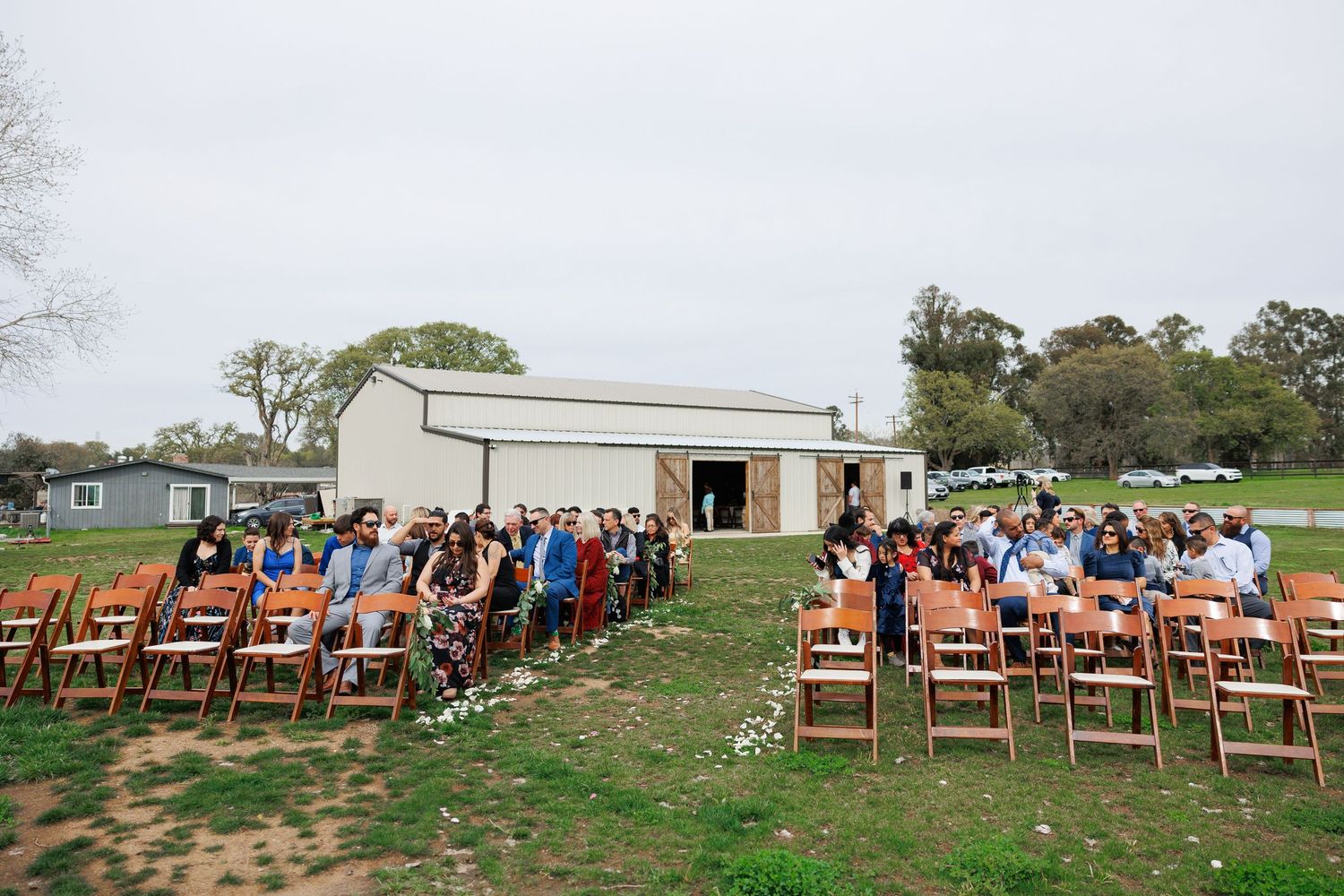 Panoramic view of wooden chairs set up for an outdoor wedding ceremony with a white barn in the background.