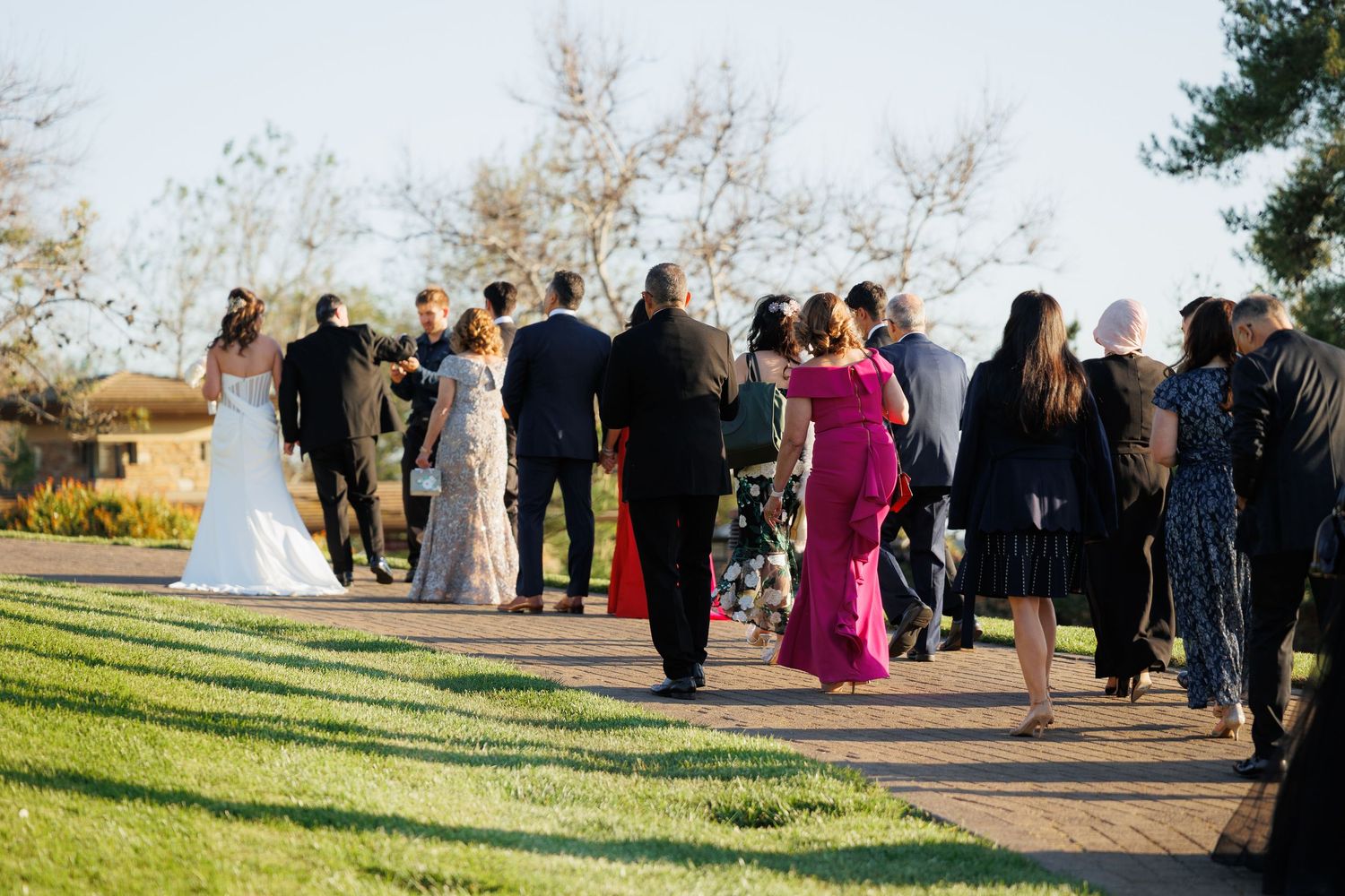 Wedding guests gather outdoors in a garden setting during a sunny afternoon ceremony.