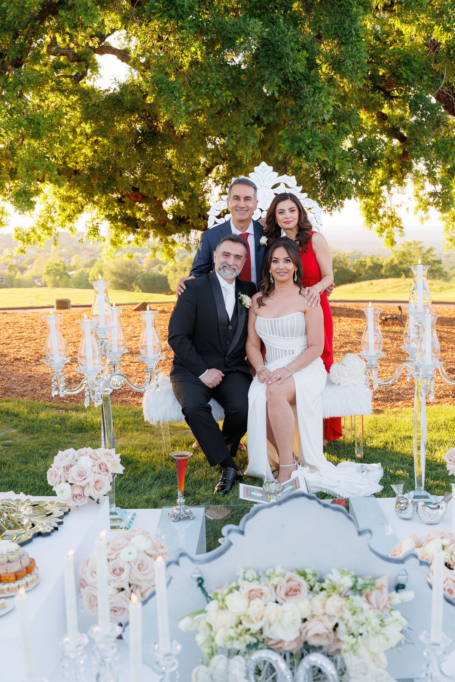 Elegant wedding dessert table setup with fountains and floral arrangements in an outdoor garden setting at sunset.