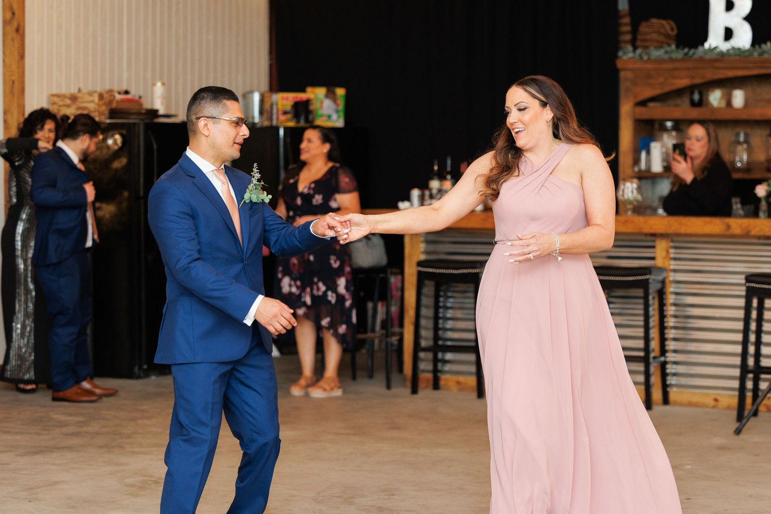 A couple in formal attire dances together at a wedding reception, with the bride wearing a pink gown.
