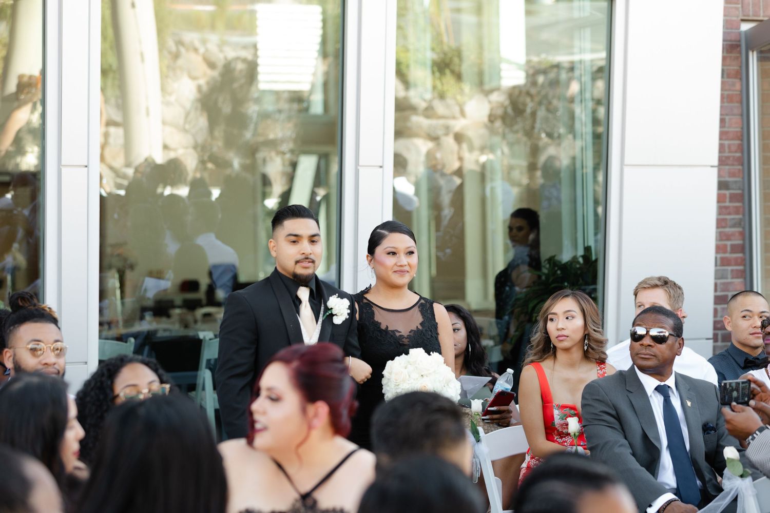 A crowd of well-dressed guests gather outside a building for what appears to be a formal event or celebration.