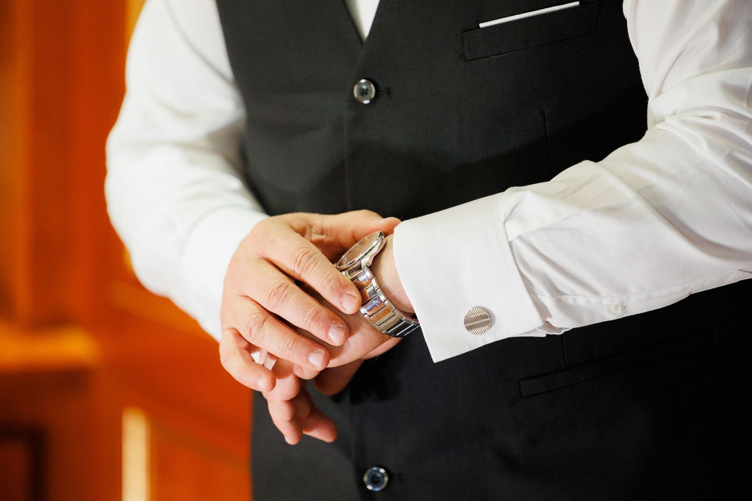 Close-up of hands buttoning a formal black vest over a crisp white dress shirt.