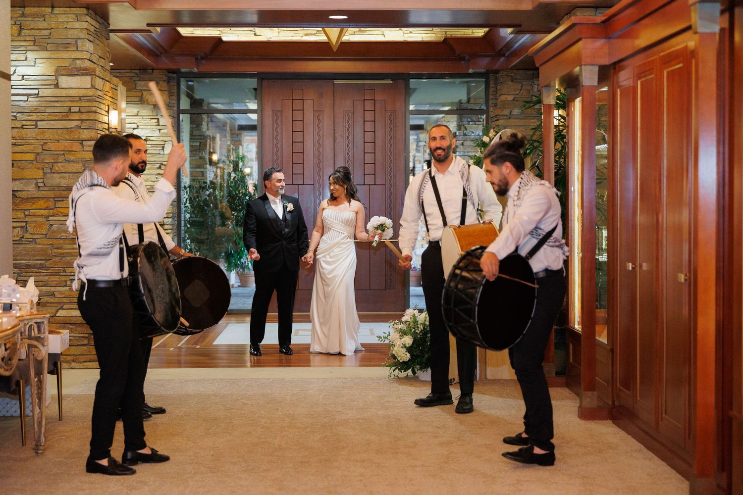 Musicians perform with string instruments at a rustic venue with exposed wooden beams and brick walls.