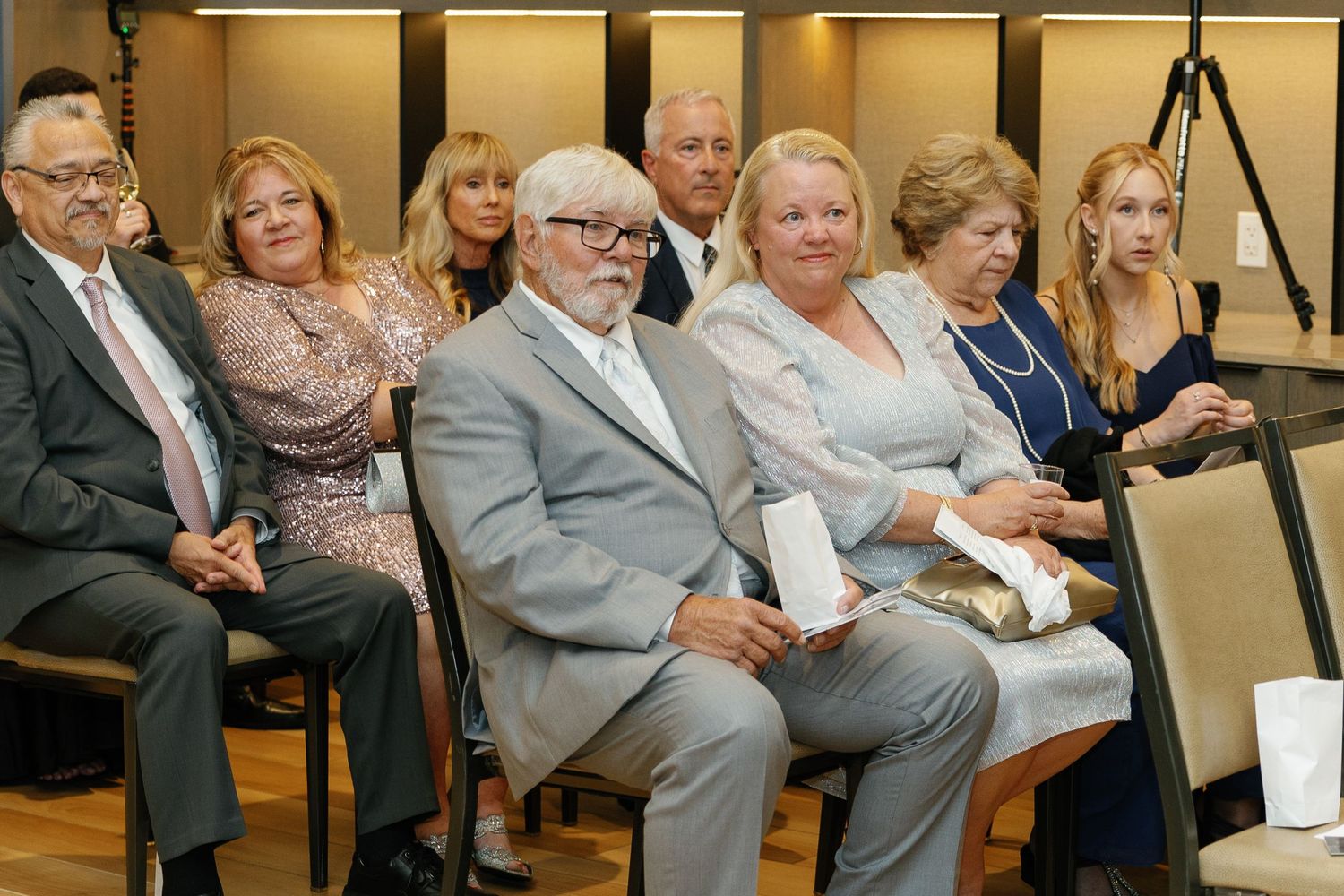 People seated in rows at an indoor event with warm lighting and formal attire.