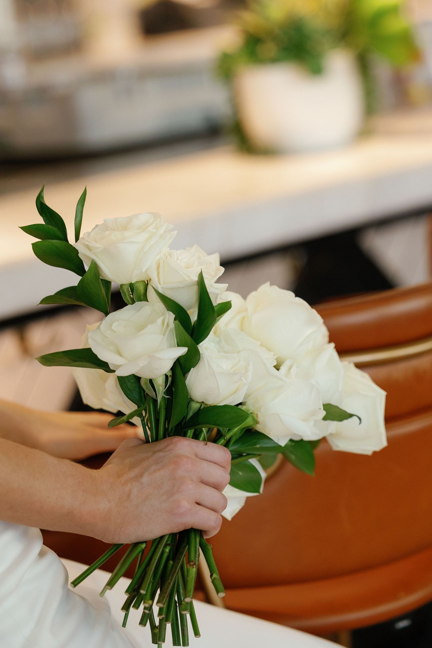 A hand arranges a bouquet of white roses with green leaves against a wooden surface.