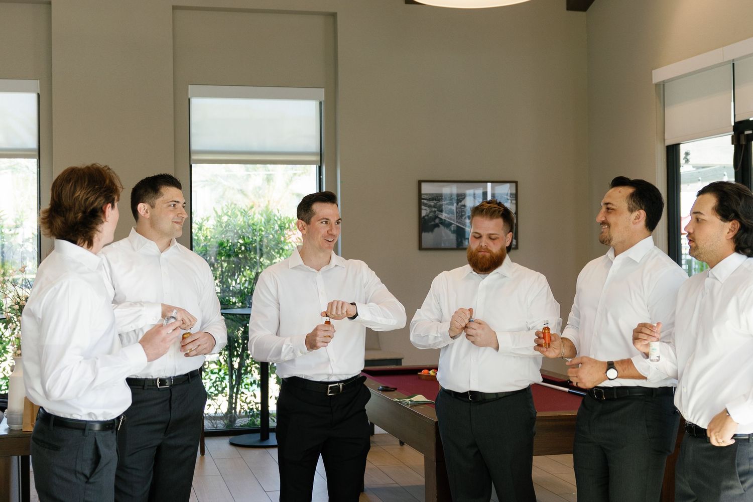 A group of groomsmen in white dress shirts gather together for conversation before a wedding ceremony.