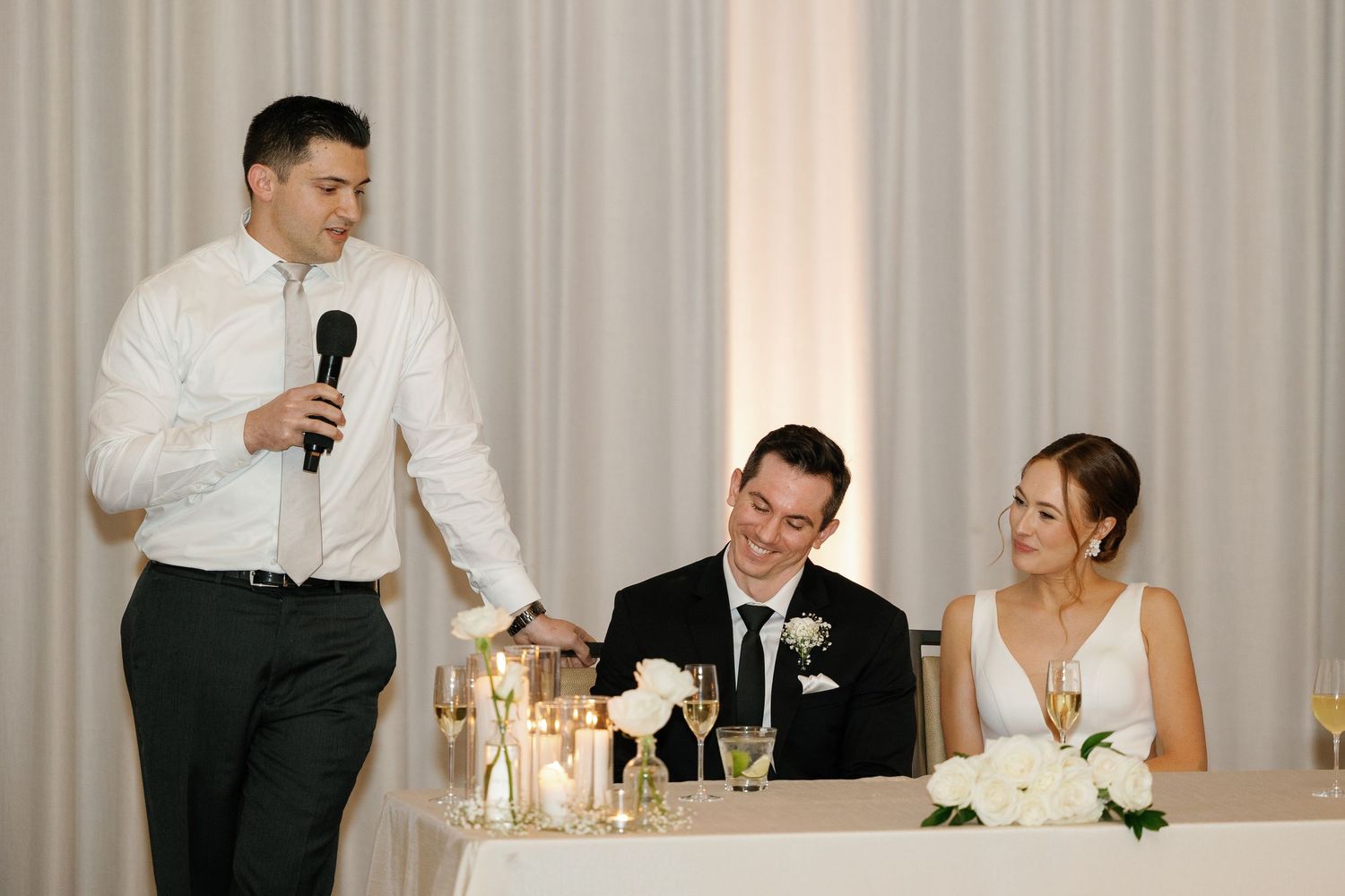 A wedding reception speech in a banquet hall with guests seated at decorated tables and candlelight.