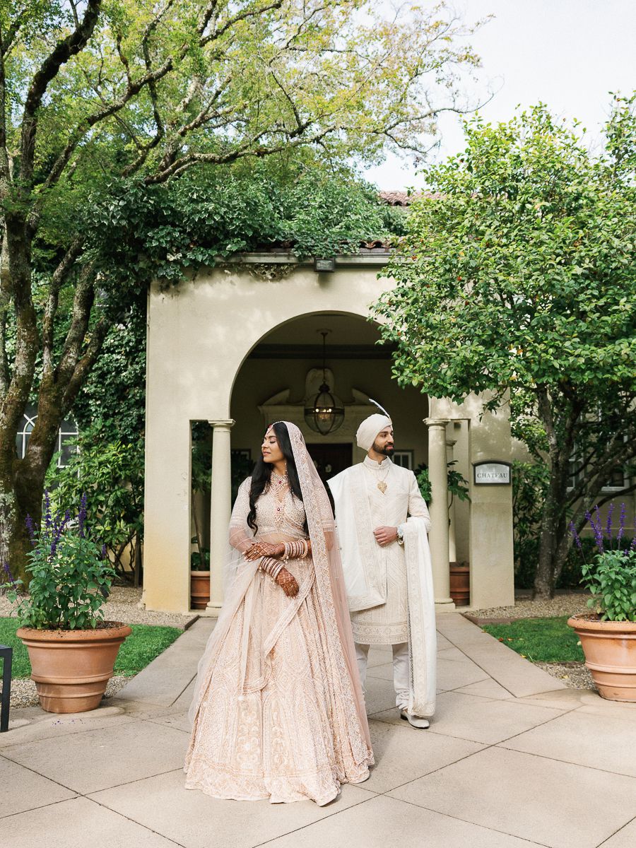 Wedding party in pastel pink outfits gathered under outdoor archways and columns.
