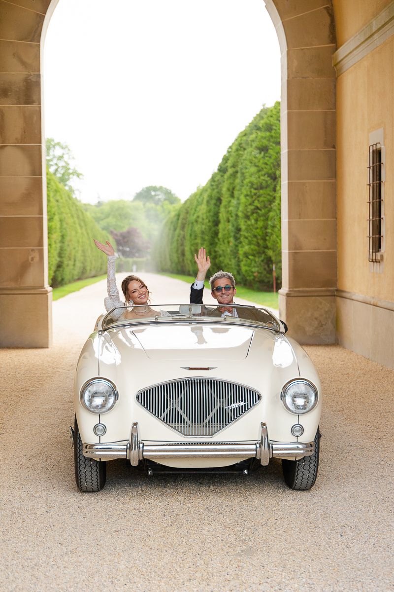 A sleek vintage white sports car with chrome details parked under elegant stone archways.