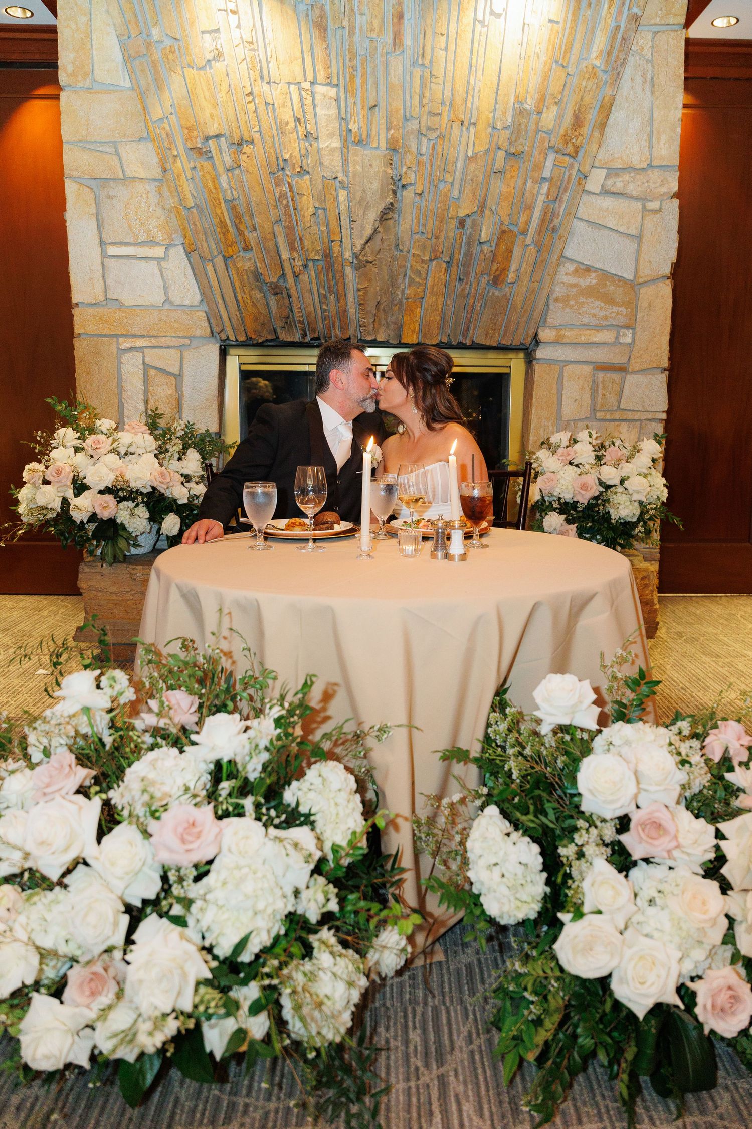 Romantic wedding reception tables decorated with elegant white hydrangeas and blush roses in a stone-walled venue.
