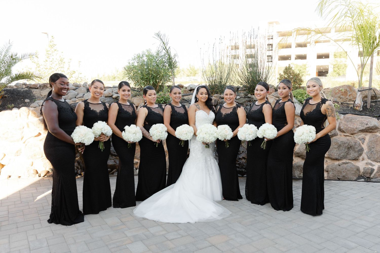 Wedding party in black and white attire poses together on stone steps for formal group photos outdoors.
