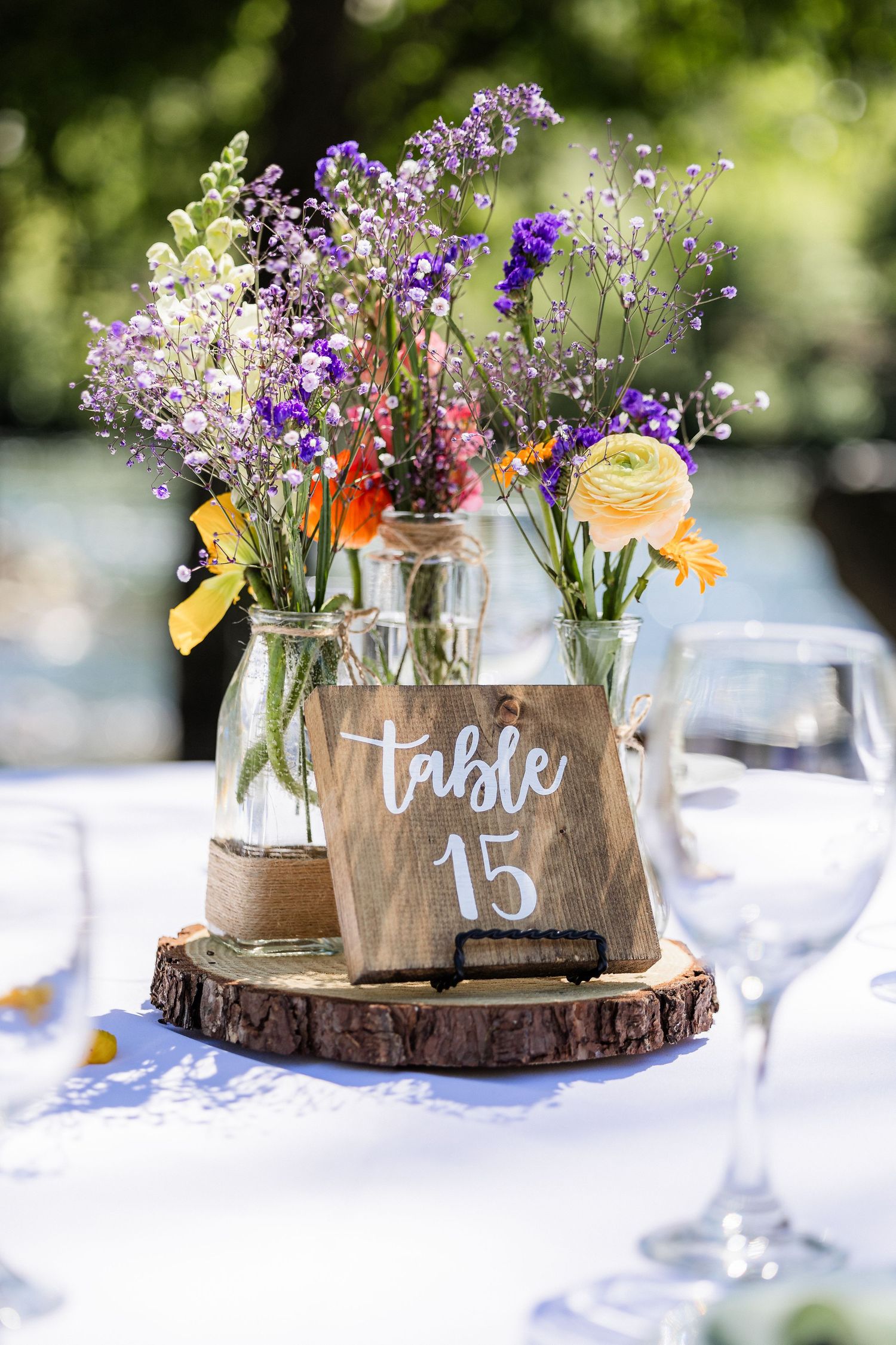 Rustic wedding table centerpieces featuring wildflowers in mason jars on wood slices with handwritten table numbers.