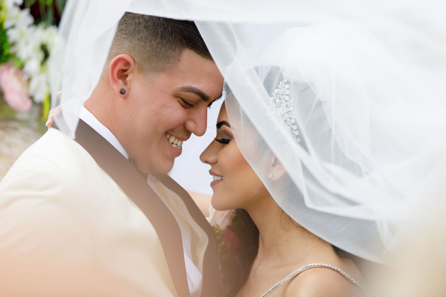 A romantic wedding couple shares an intimate moment under a white veil during their special day.