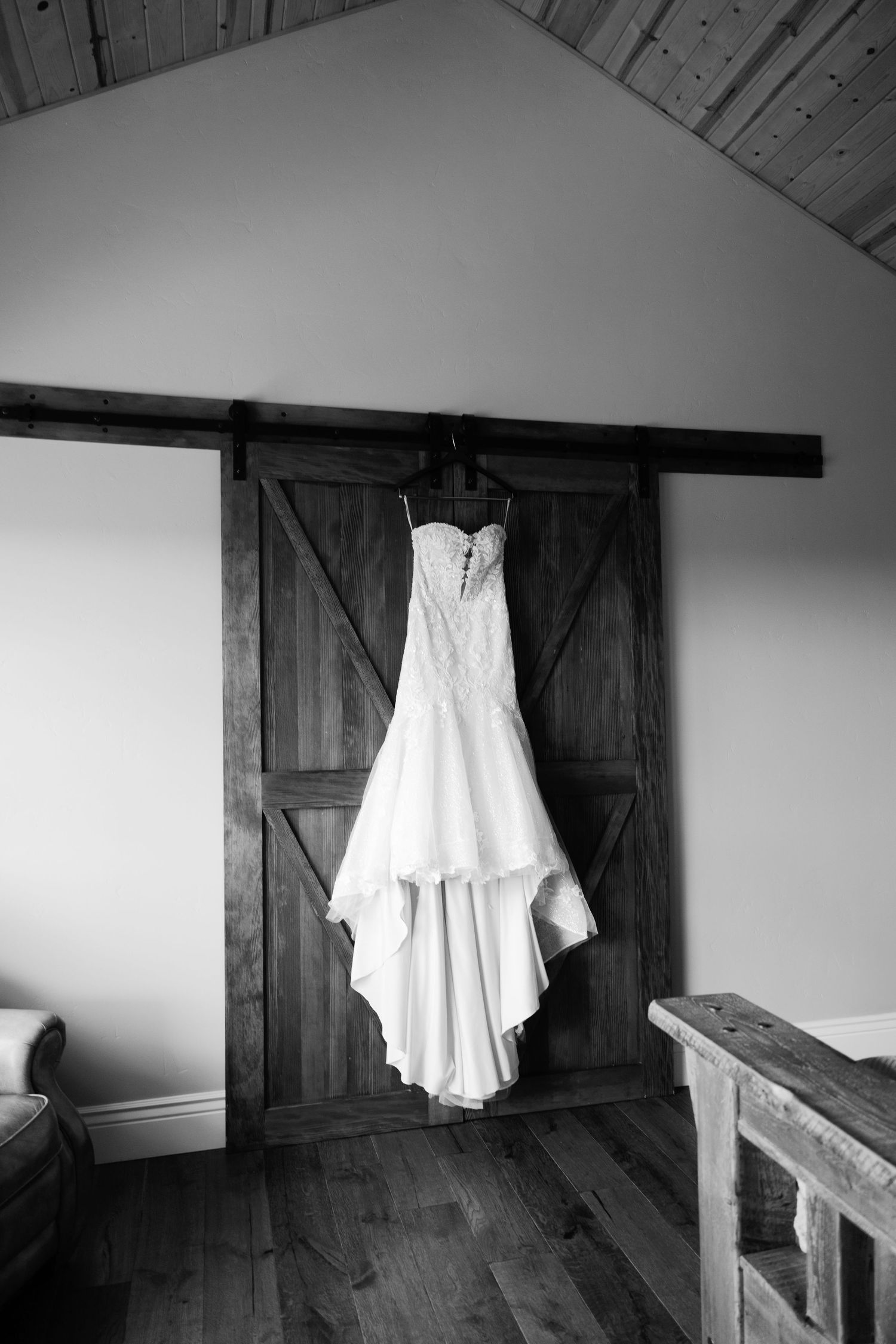 Black and white photo of a wedding dress hanging on rustic barn doors in an attic space.