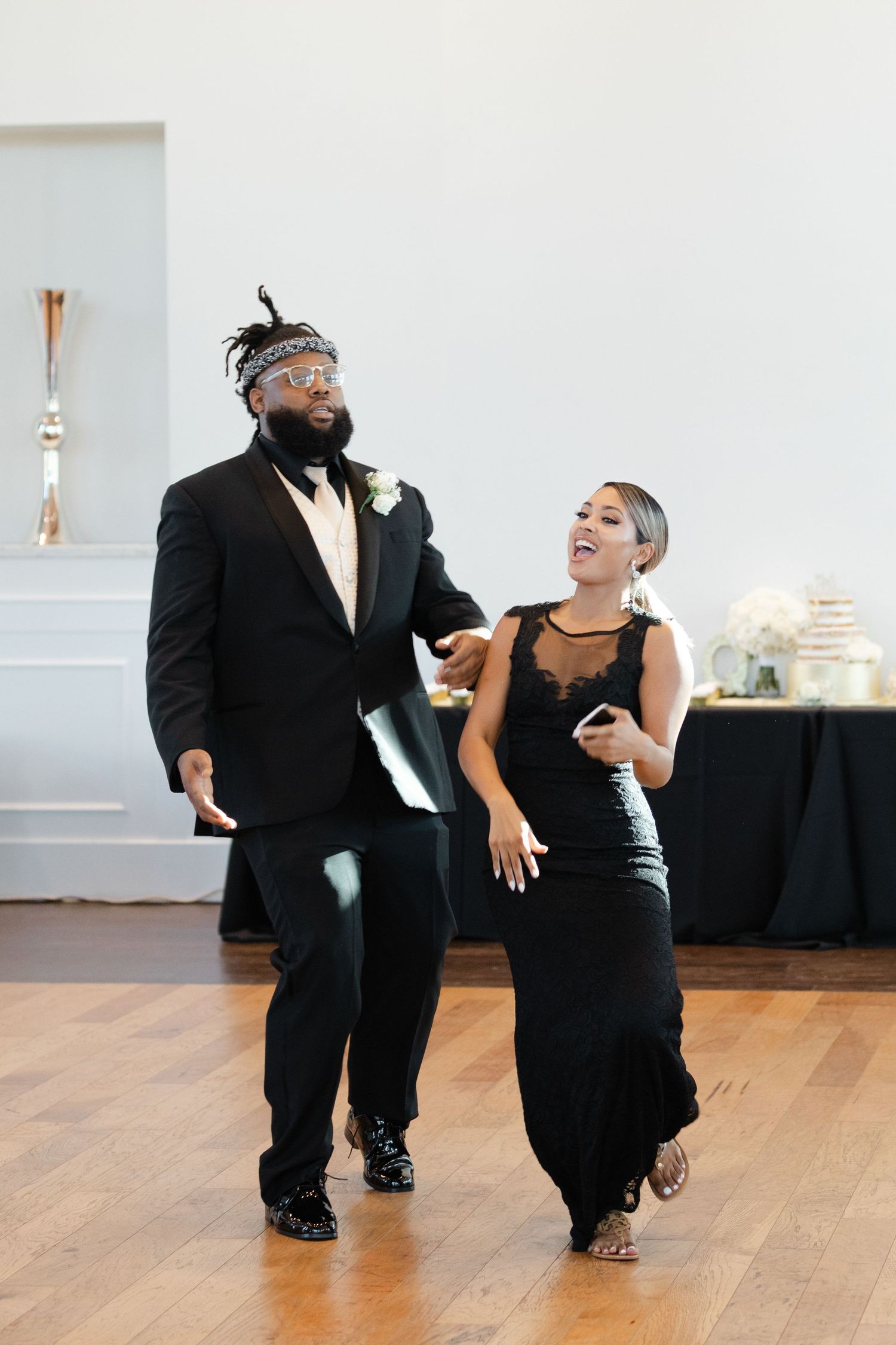 Couple in elegant black attire dancing together on wooden floor at formal event.
