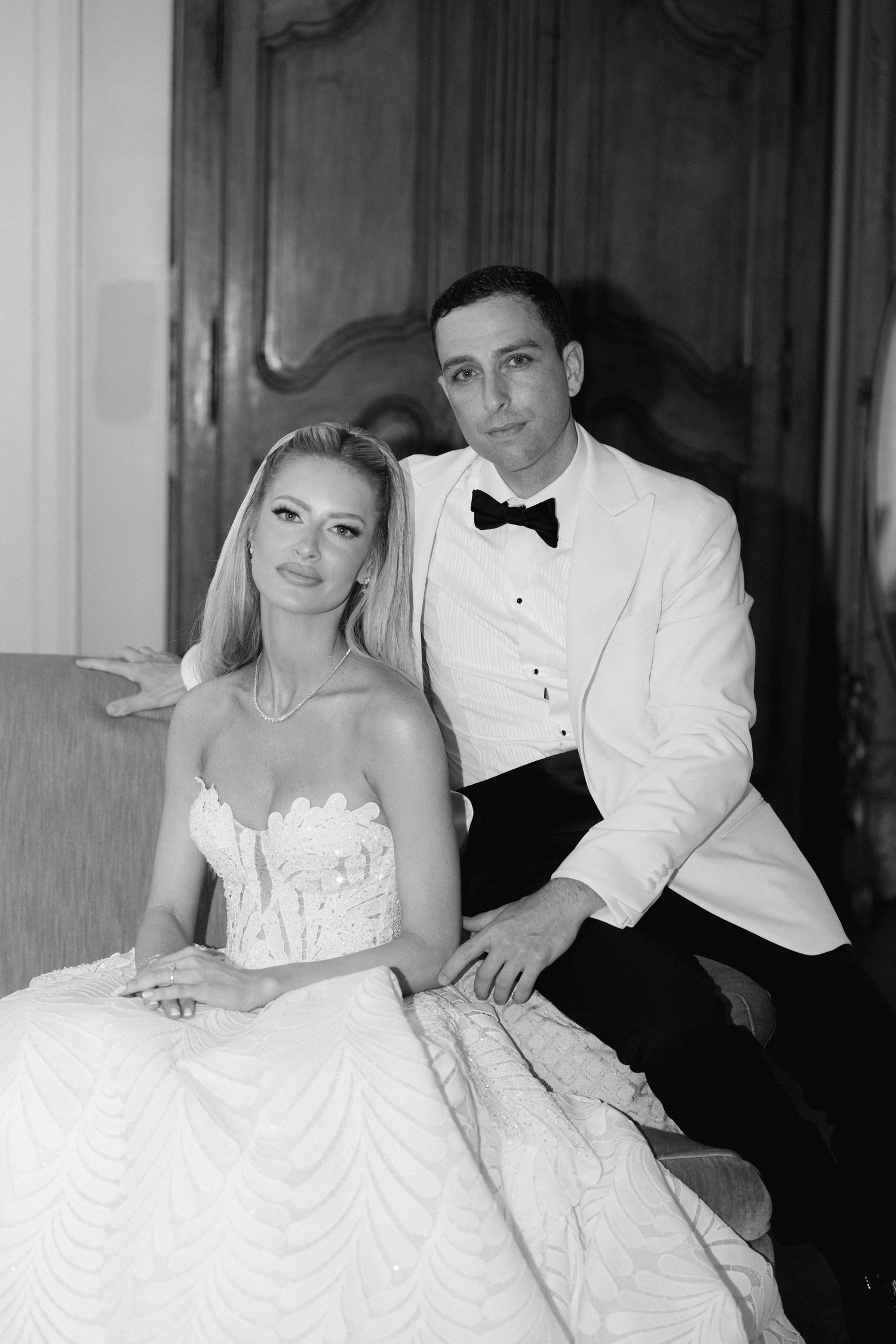 A black and white wedding photo showing a couple in formal attire, with the bride in a white gown and groom in white jacket.