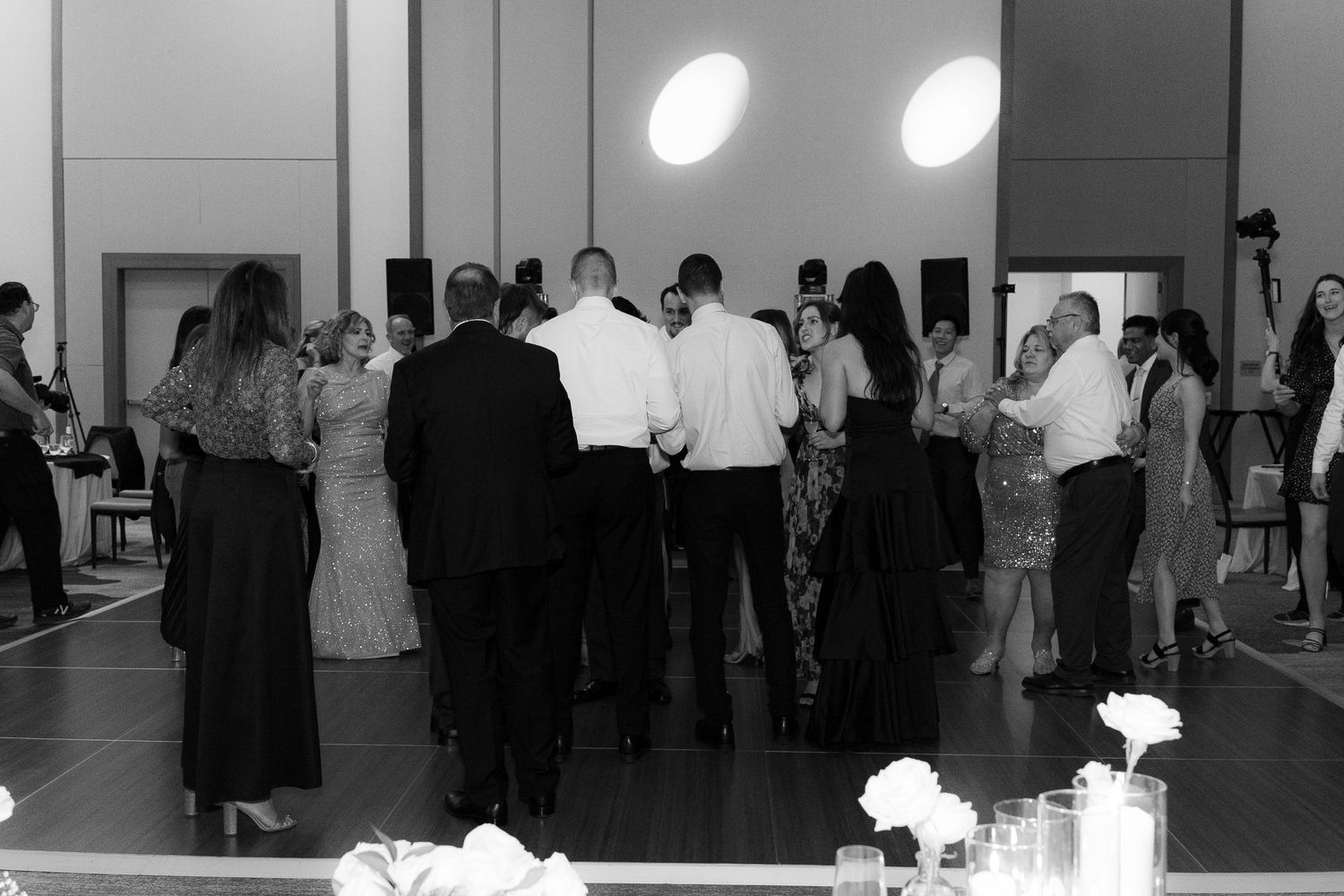 A group of people gather in a large indoor space with white walls and polished floors for a social event.