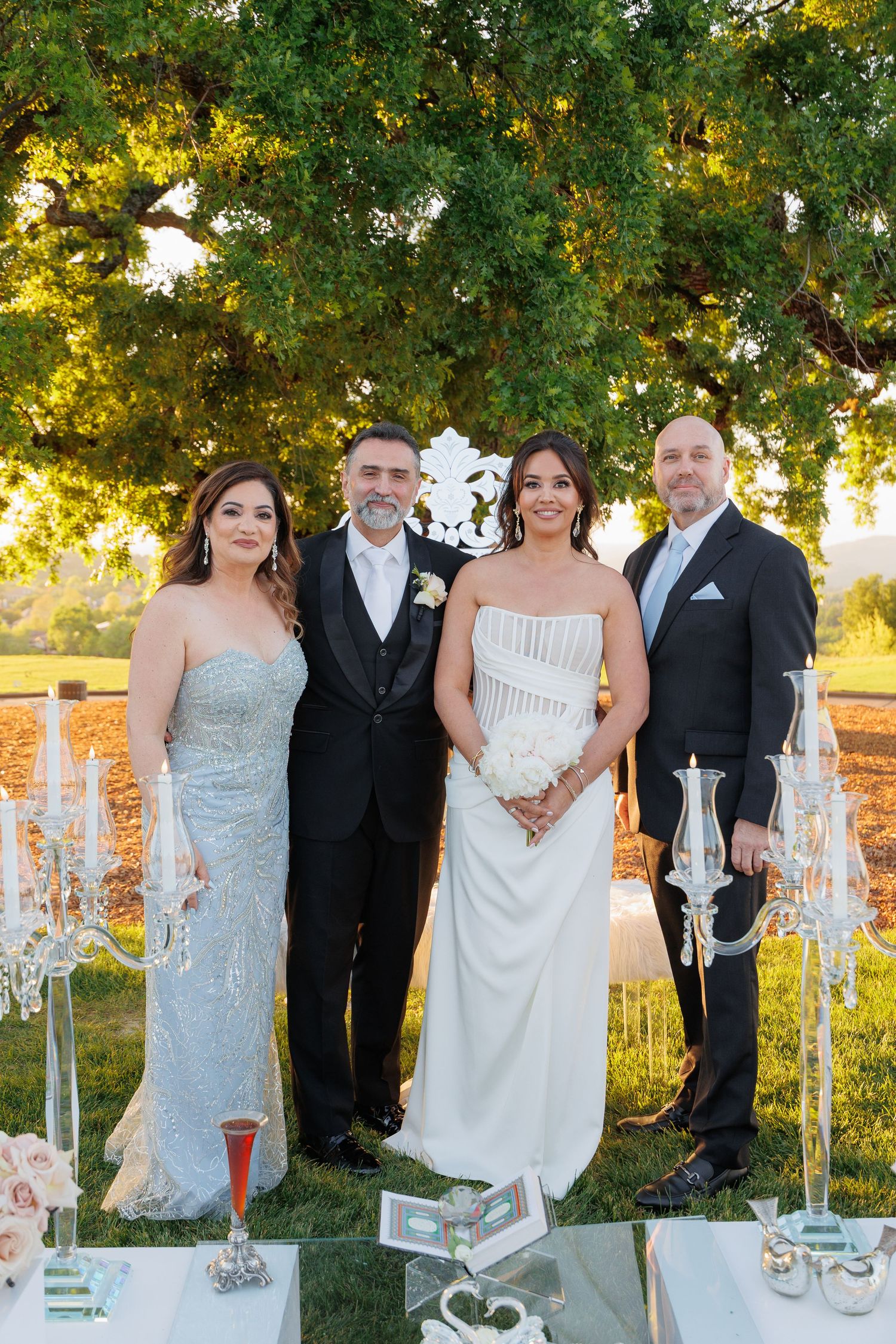 Wedding party poses outdoors at sunset with elegant white candle holders and decorative elements in the foreground.