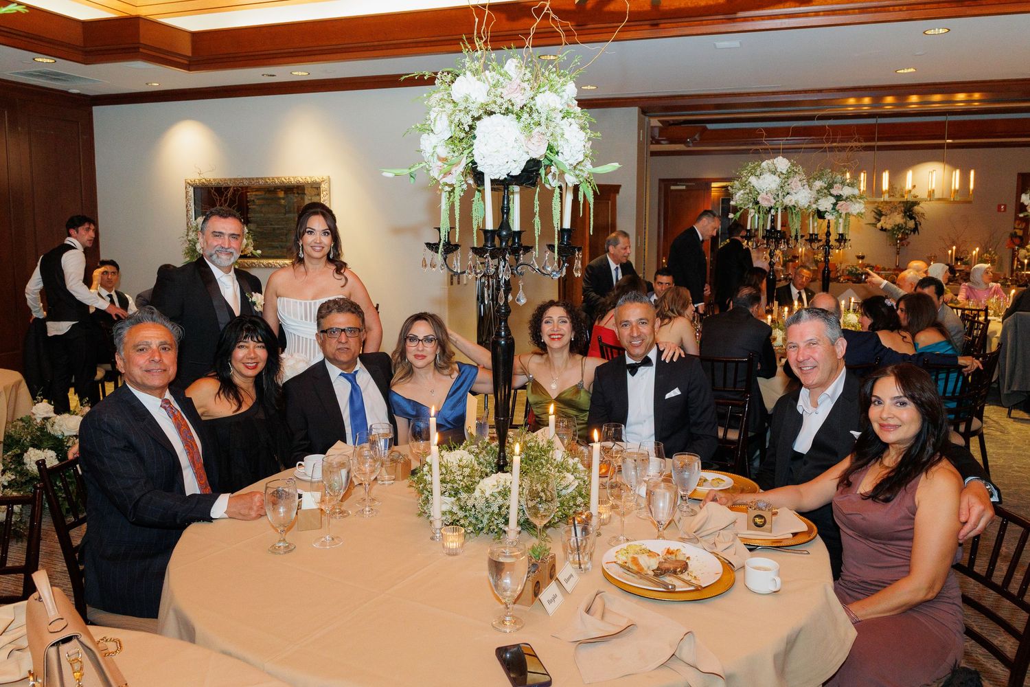 Wedding reception guests seated at elegant banquet tables with white floral centerpieces in a luxurious dining room.