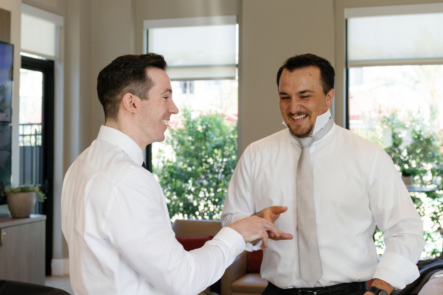 Two people in white dress shirts laugh and interact during a business conversation in a bright office setting.