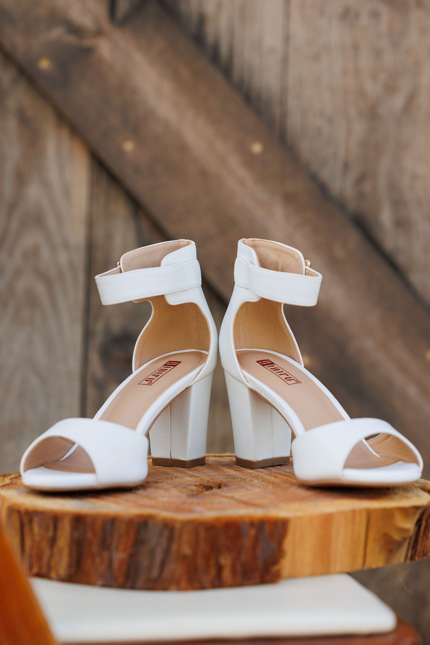 White wedding shoes with low block heels displayed on a rustic wooden surface from multiple angles.