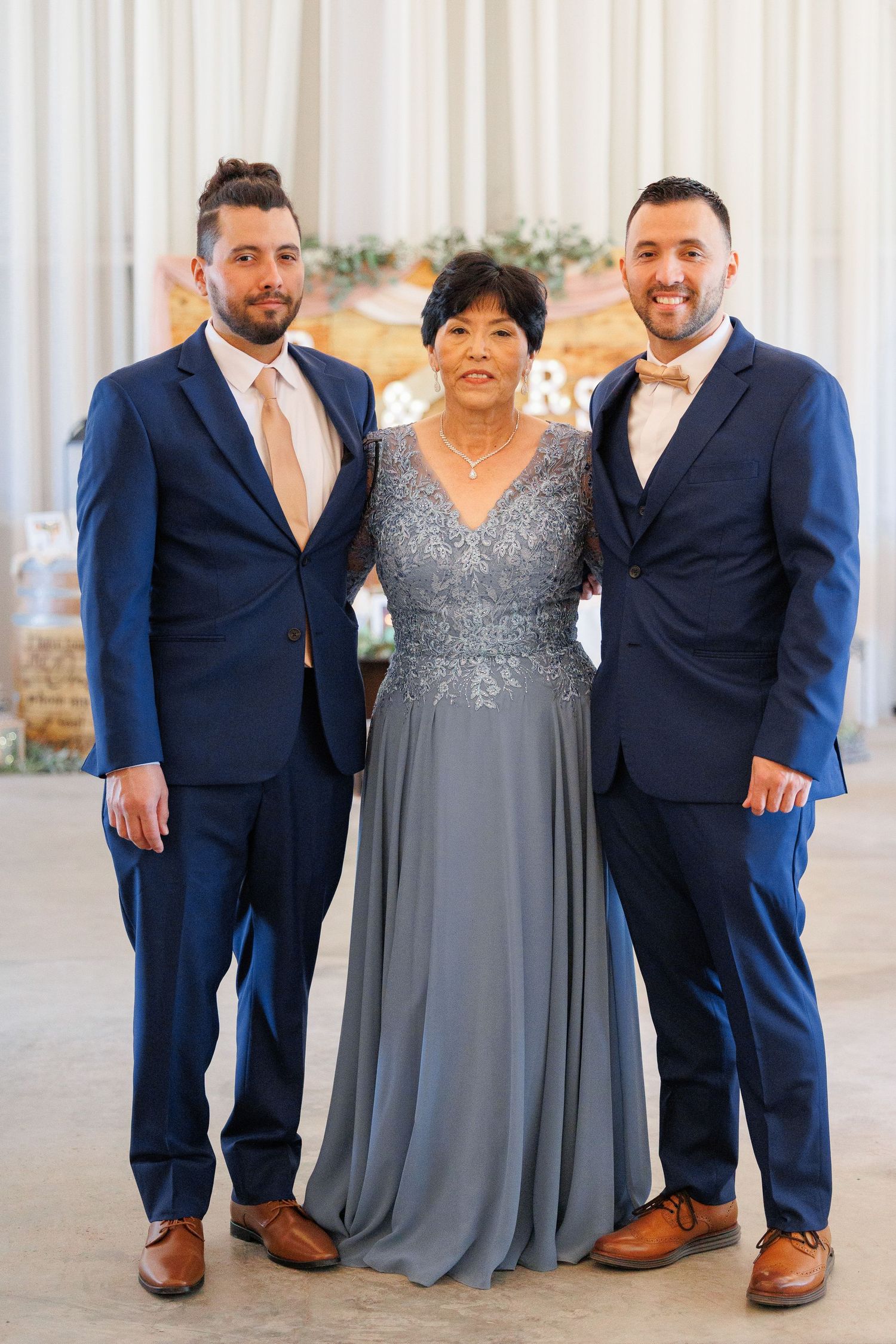 Three people pose formally at an event, with two men in navy suits and a woman in a sparkly gray evening gown.