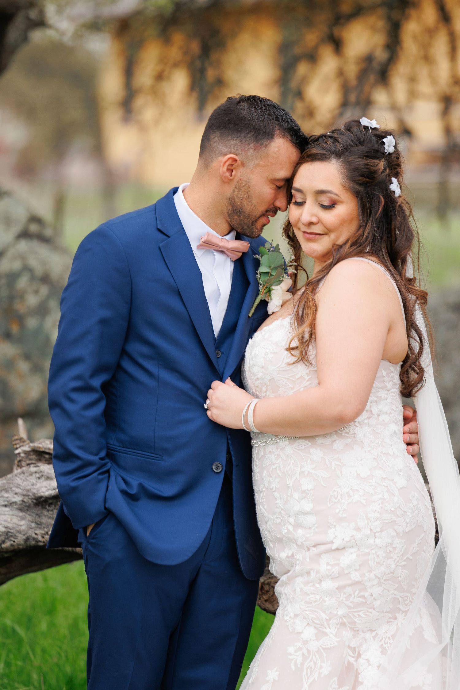 A romantic wedding couple in a navy suit and white lace dress share intimate moments in an outdoor setting.