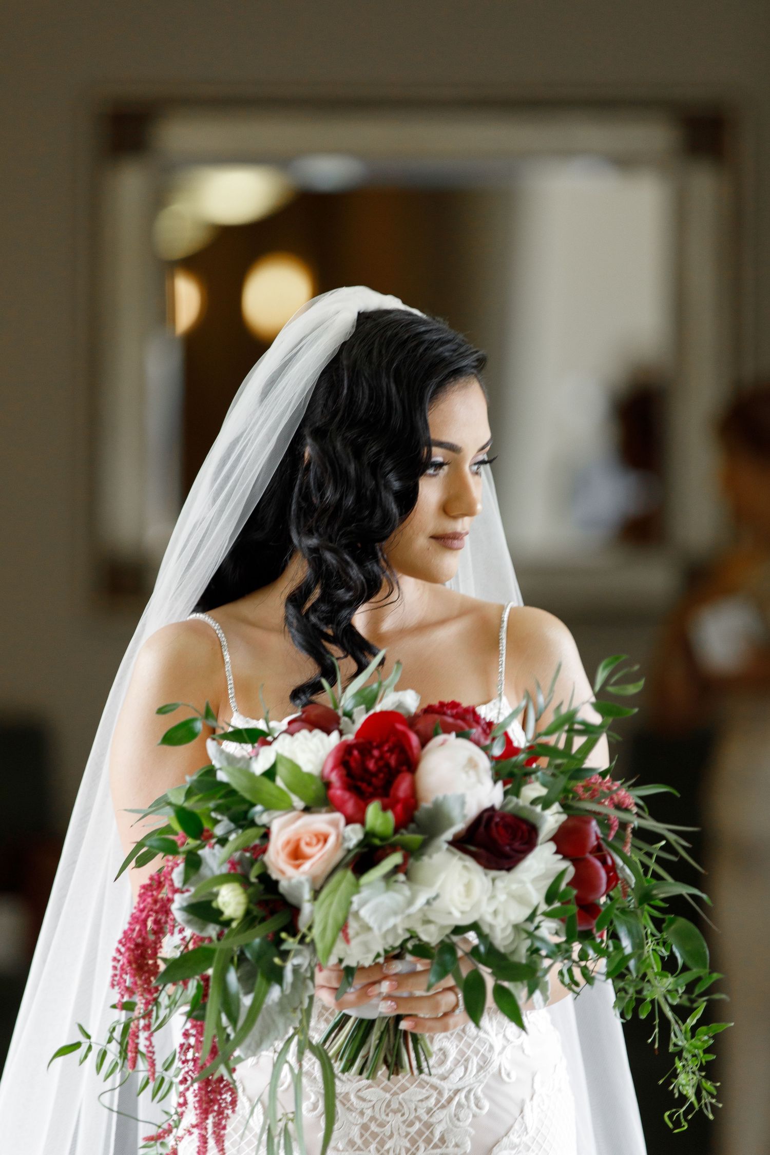 A bride in a white lace gown holds a stunning burgundy and blush bouquet with cascading greenery.