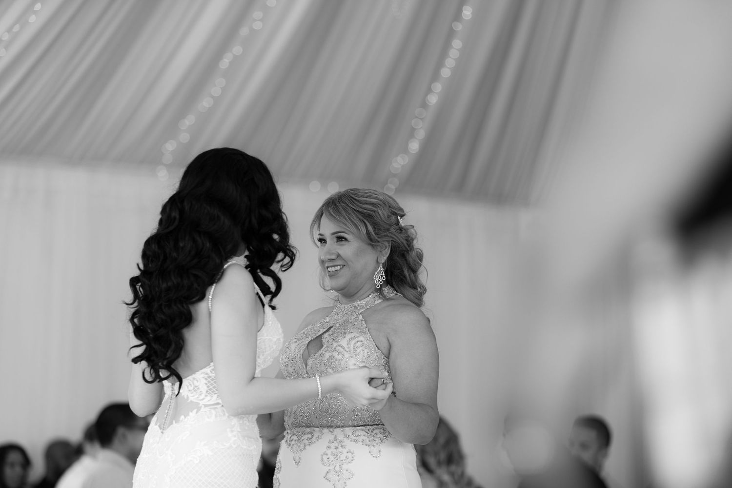 Two people in elegant white dresses share an emotional moment during a wedding reception.