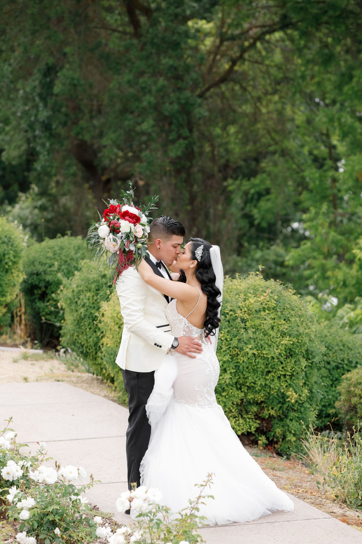 Romantic couple in wedding attire embracing in a lush garden setting with natural greenery in the background.