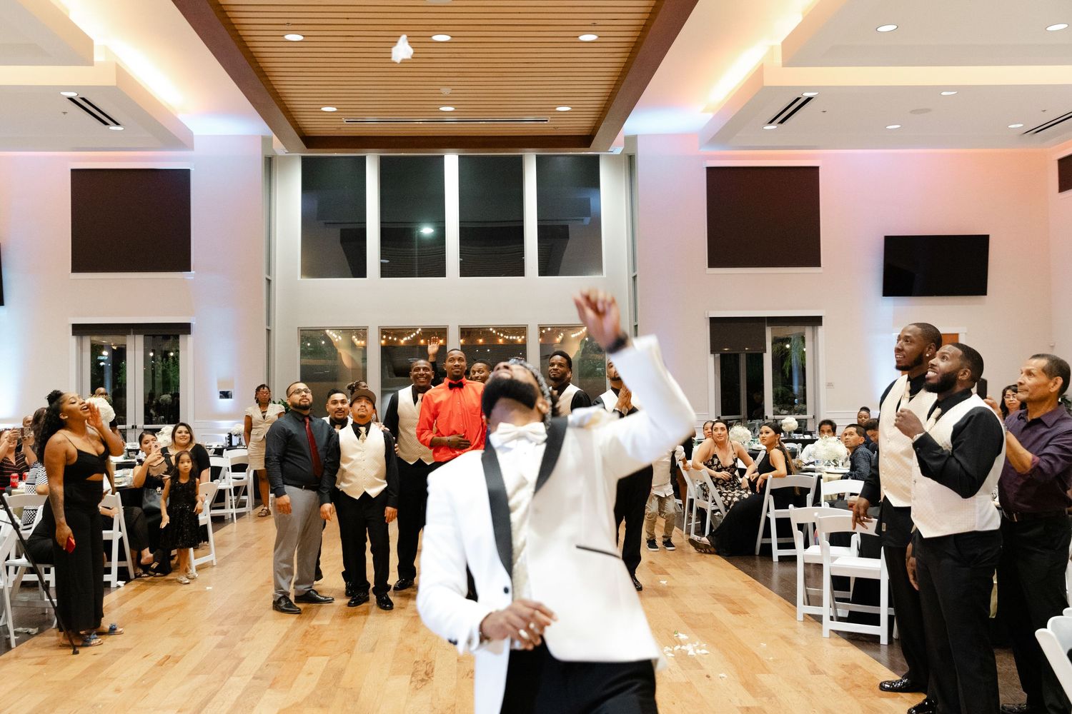 Wedding reception guests dance and celebrate on a large dance floor in an elegant banquet hall with wood paneled ceiling.