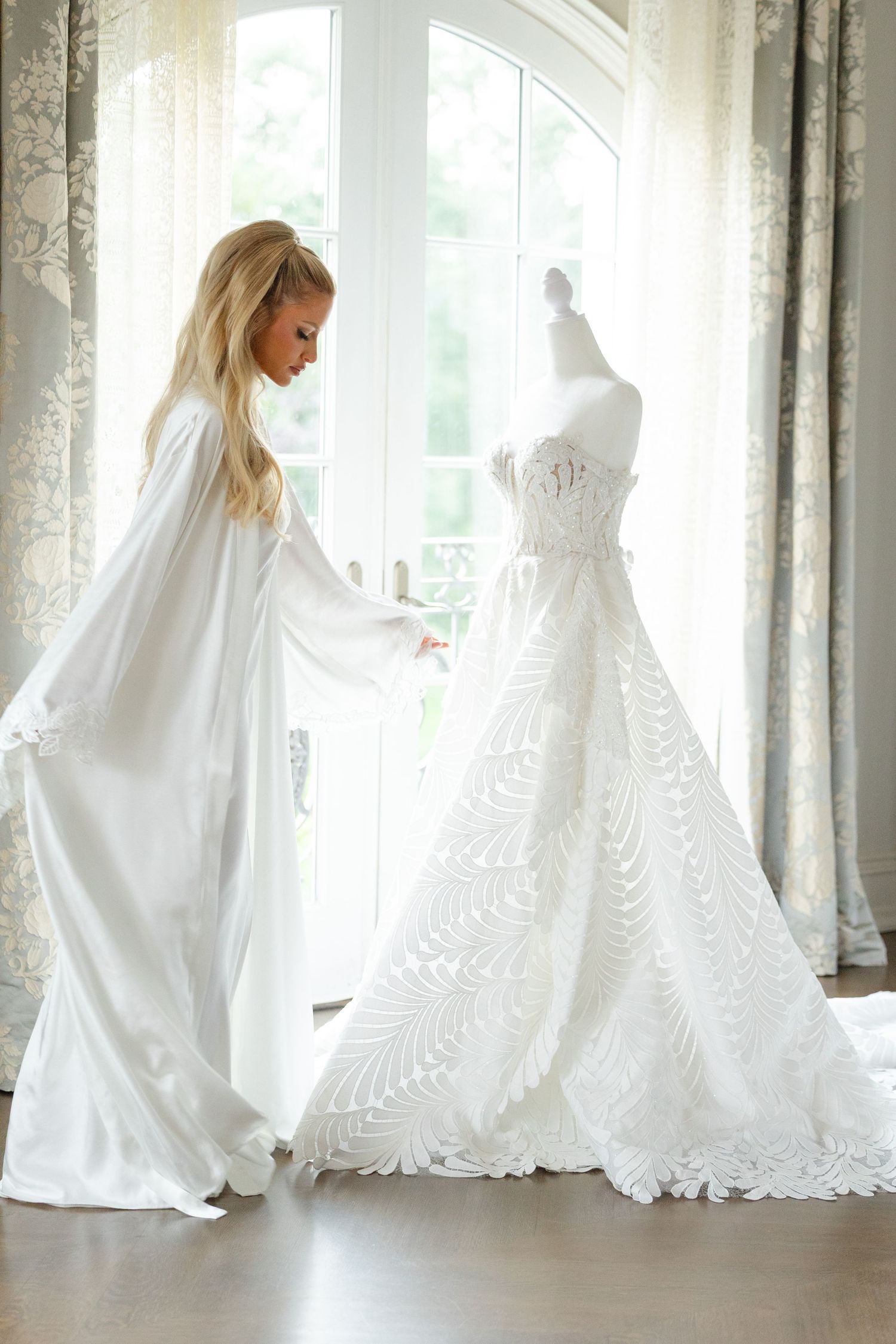 Elegant white wedding dresses displayed in a bright sunlit room with flowing fabrics and delicate lace details.