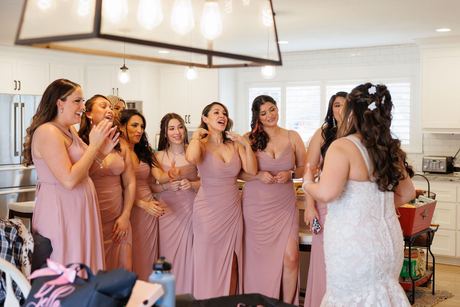 A group in dusty rose bridesmaid dresses reacts emotionally during a wedding celebration.