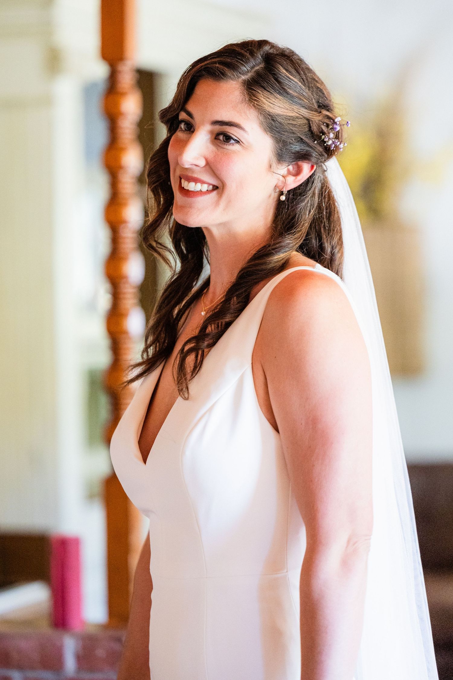 Bride wearing elegant white sleeveless wedding dress smiles joyfully with hair styled in romantic waves.