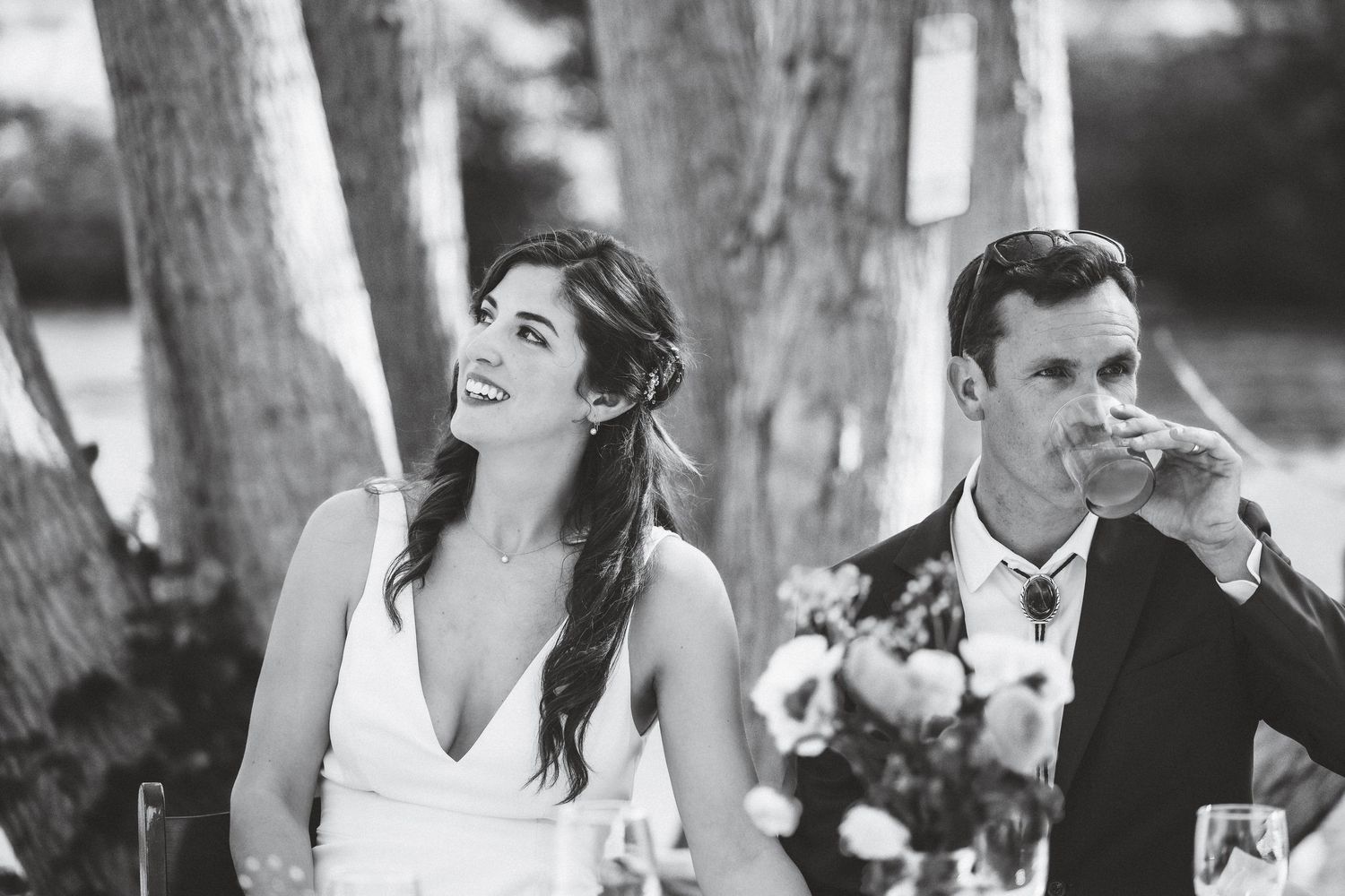 Black and white photo series showing candid wedding moments with the couple and guests laughing together outdoors.