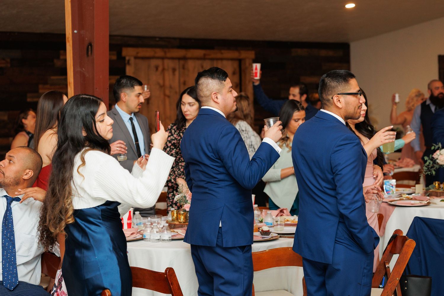 Wedding guests dance and socialize during a reception in a warmly lit indoor venue.