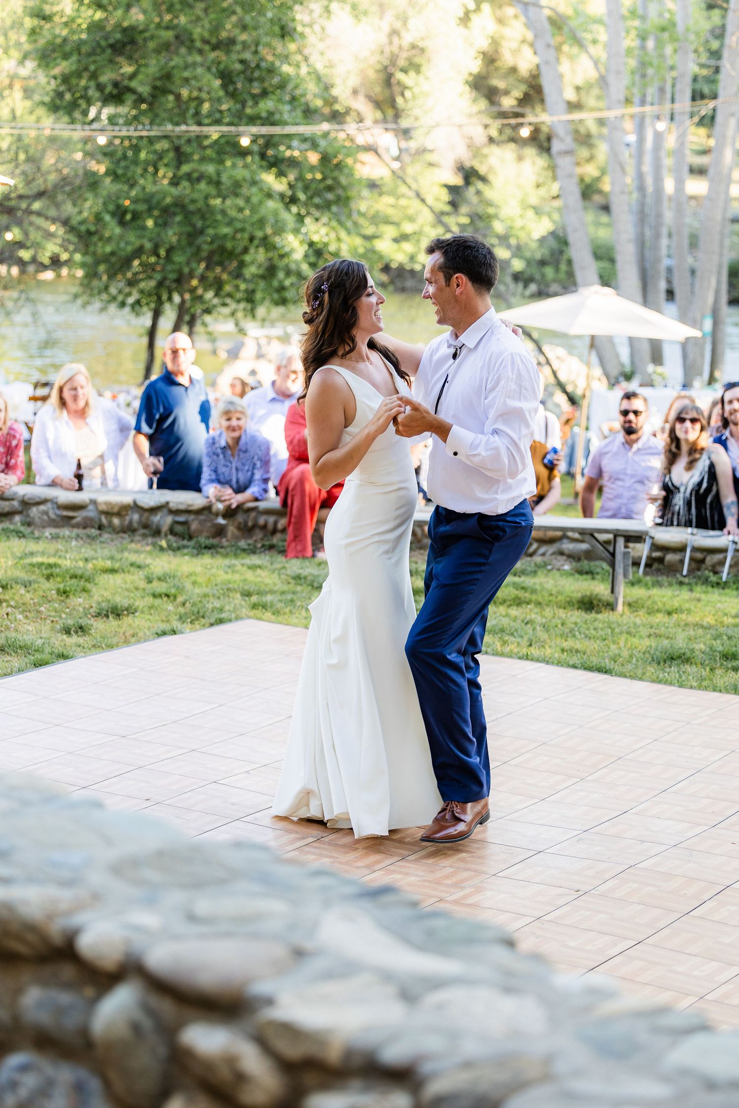 A couple shares a romantic dance moment during an outdoor wedding reception on a paved patio area surrounded by greenery.