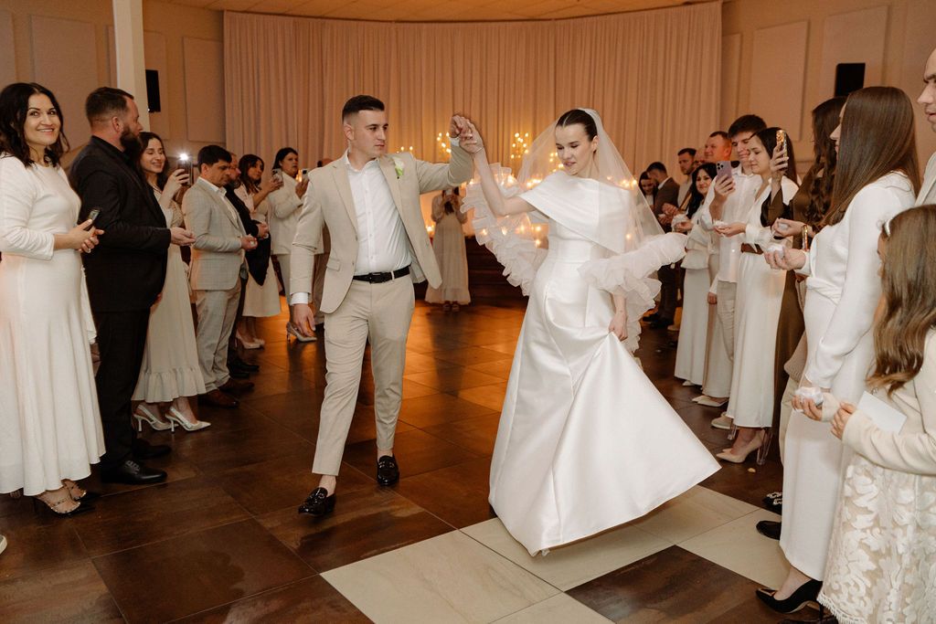 Wedding guests in formal attire dance and celebrate in an elegantly decorated ballroom.