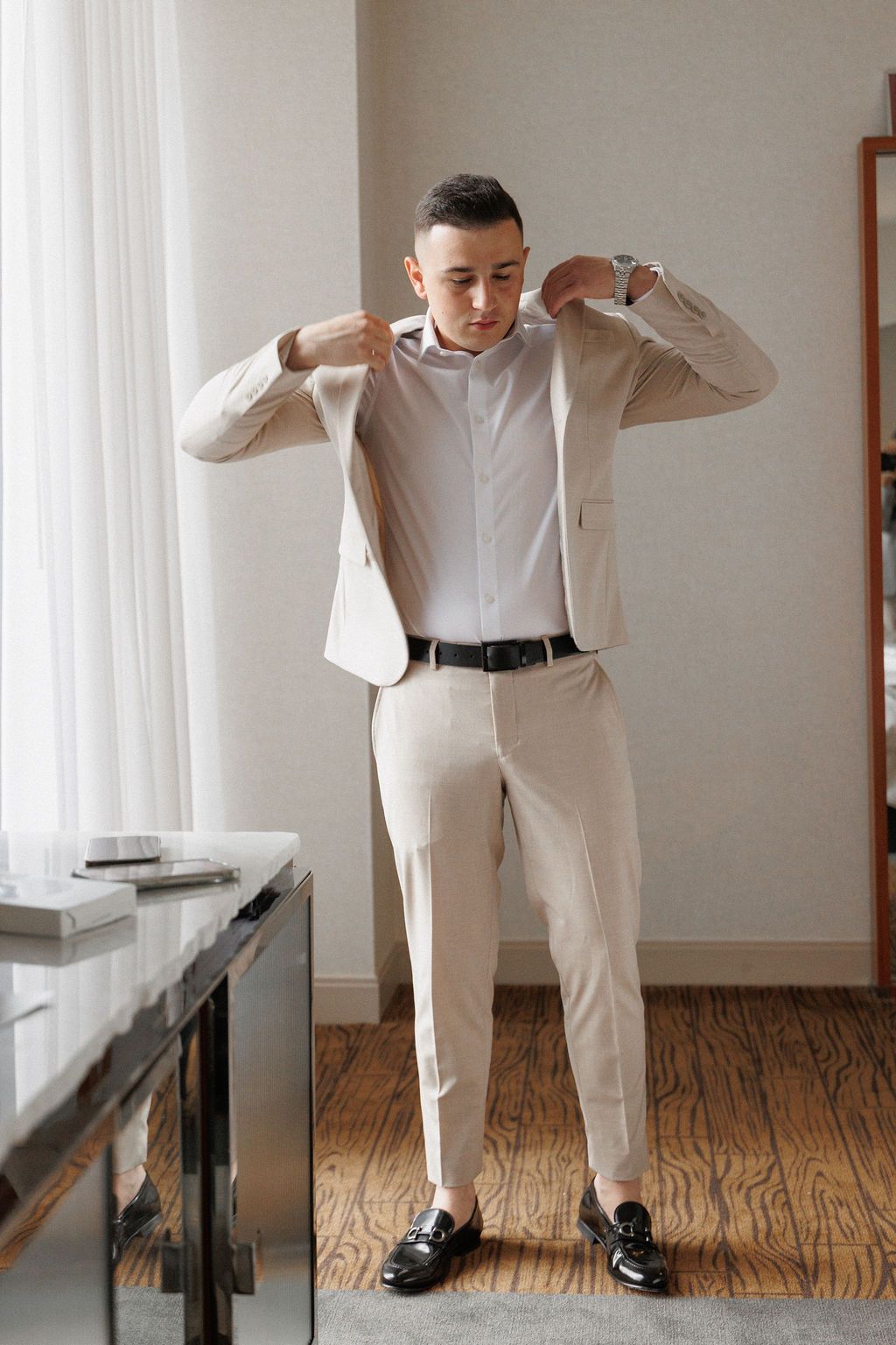 Series of photos showing someone in a beige suit and white shirt getting dressed for a formal occasion.