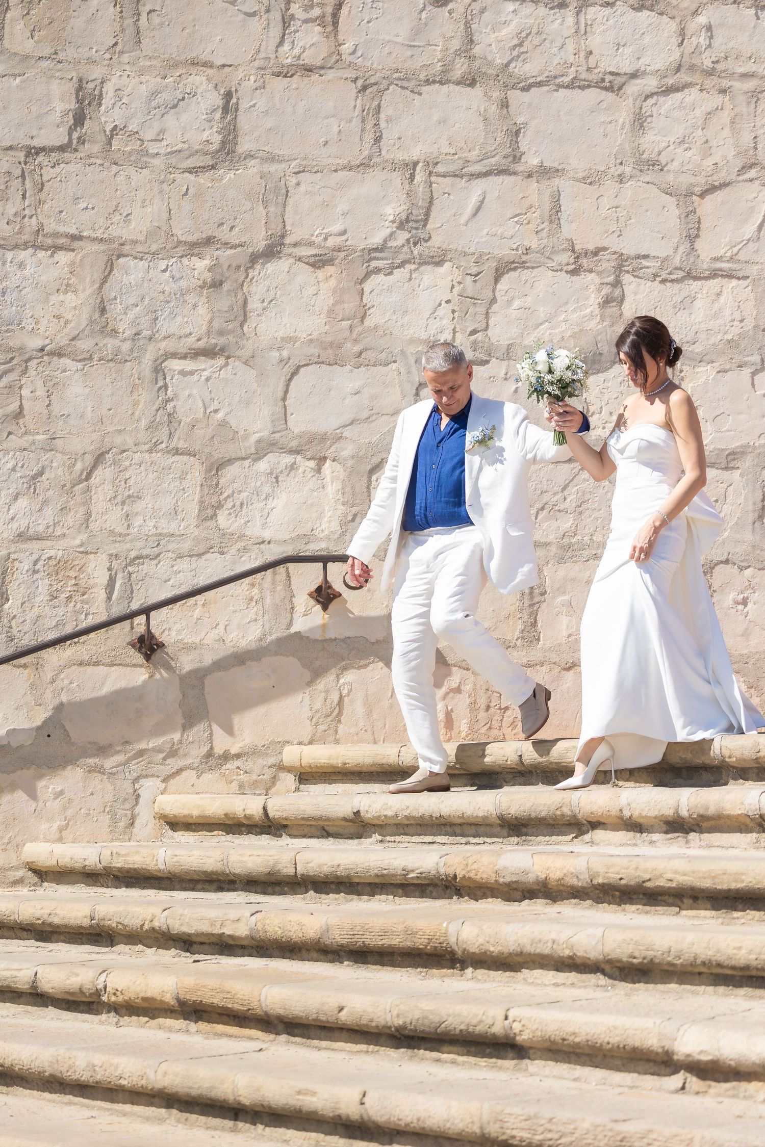 A couple descends stone steps against a rustic wall during their wedding ceremony.