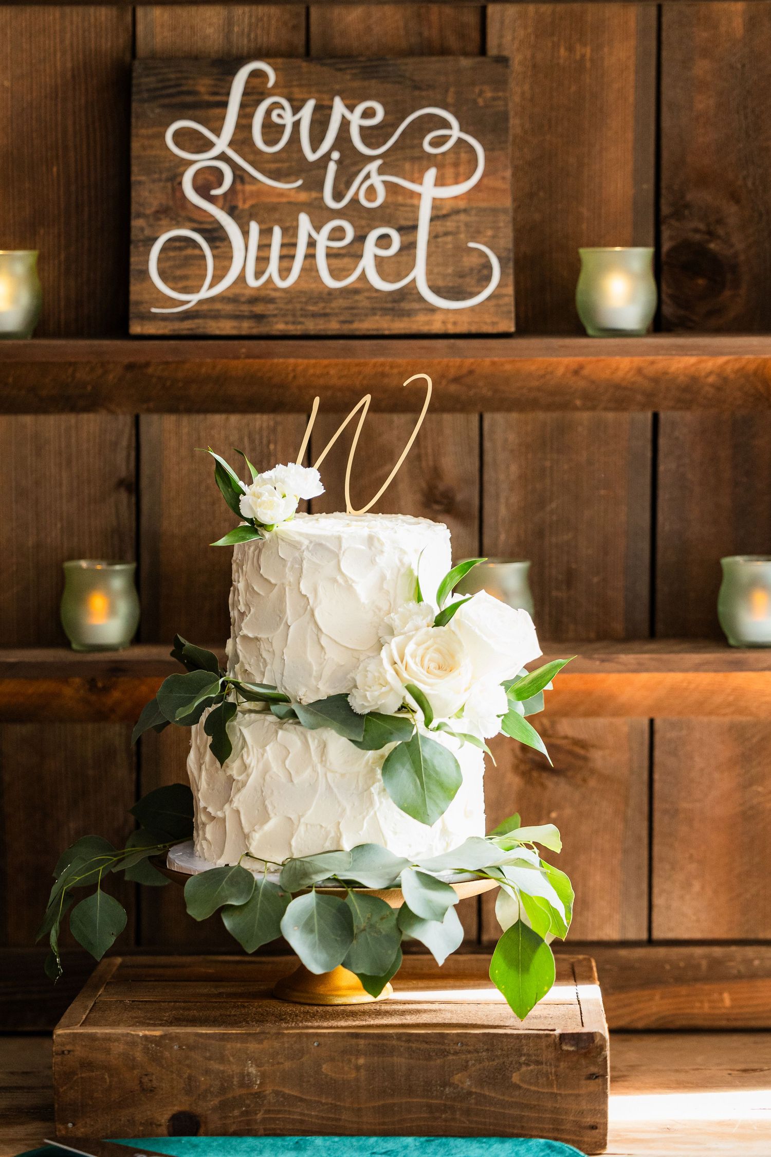 Rustic wooden wedding display with white cake and 'Love is Sweet' signage.