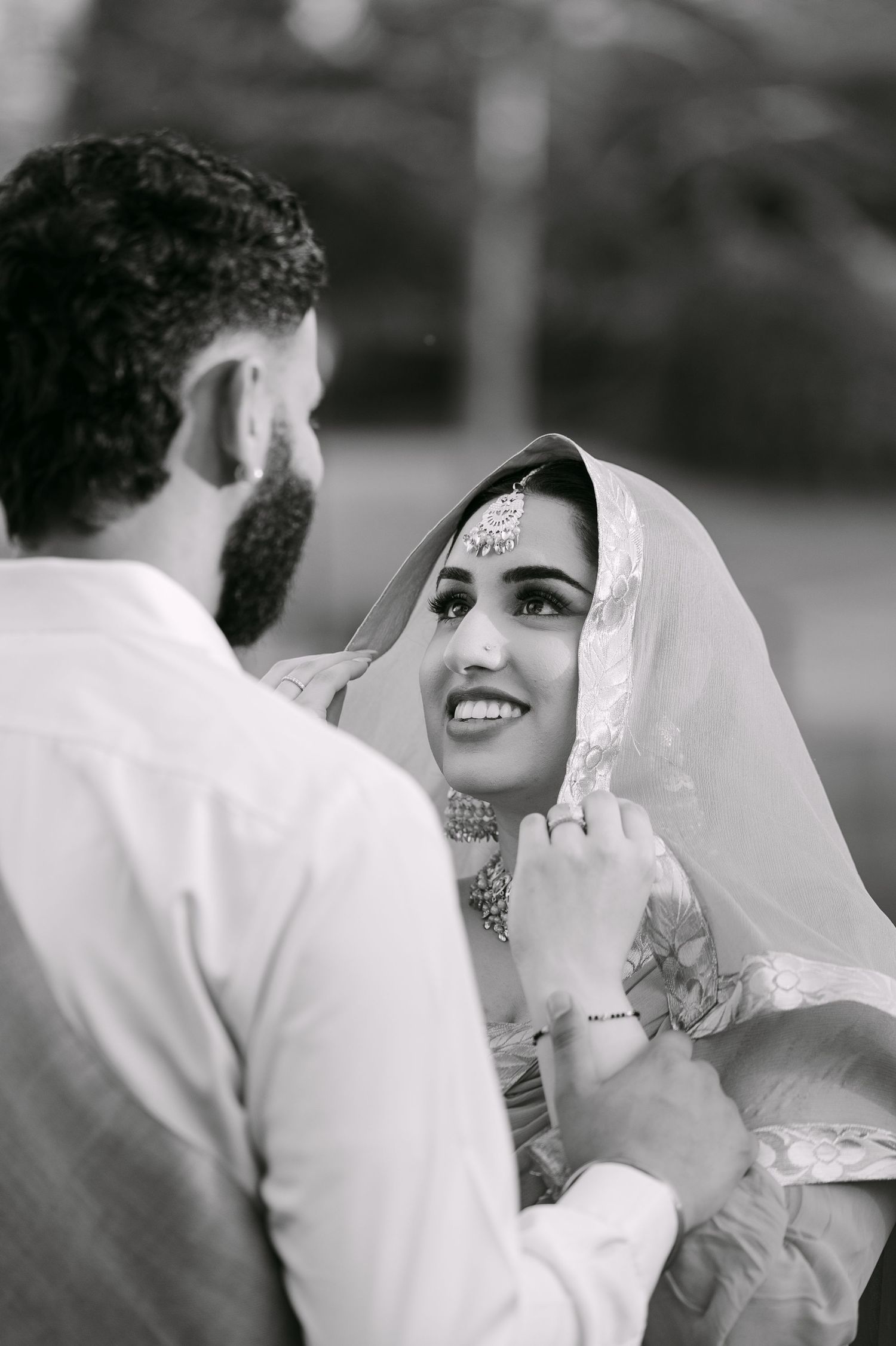 Black and white wedding photo showing tender moment between couple as bride smiles wearing traditional Indian bridal attire.