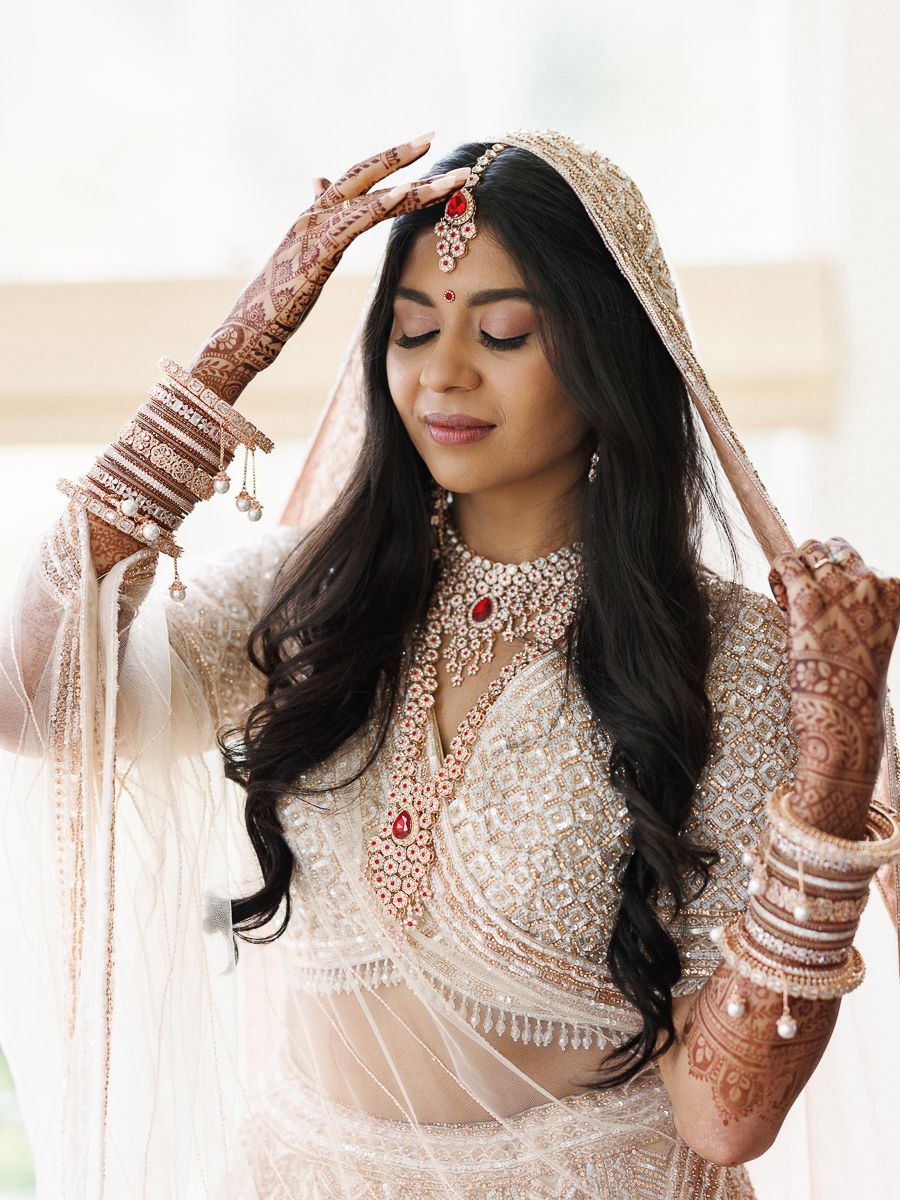 Close-up details of intricate bridal jewelry and henna adorned hands in traditional South Asian wedding attire.