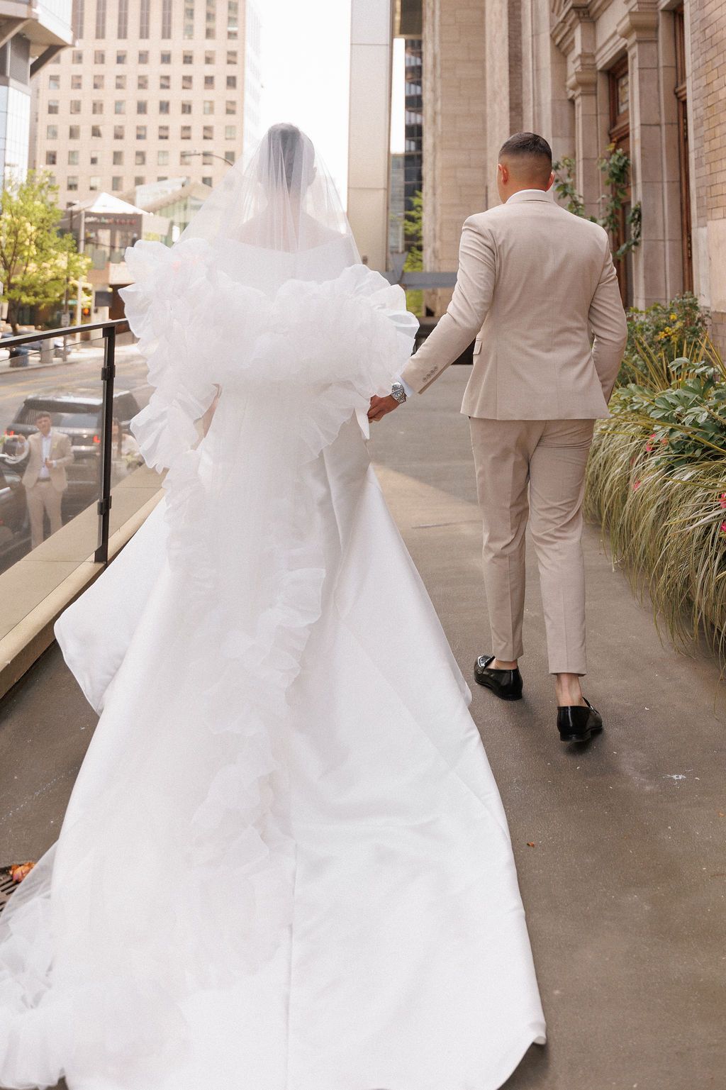 An elegant wedding couple walks along a columned walkway with the bride's flowing white dress trailing behind.