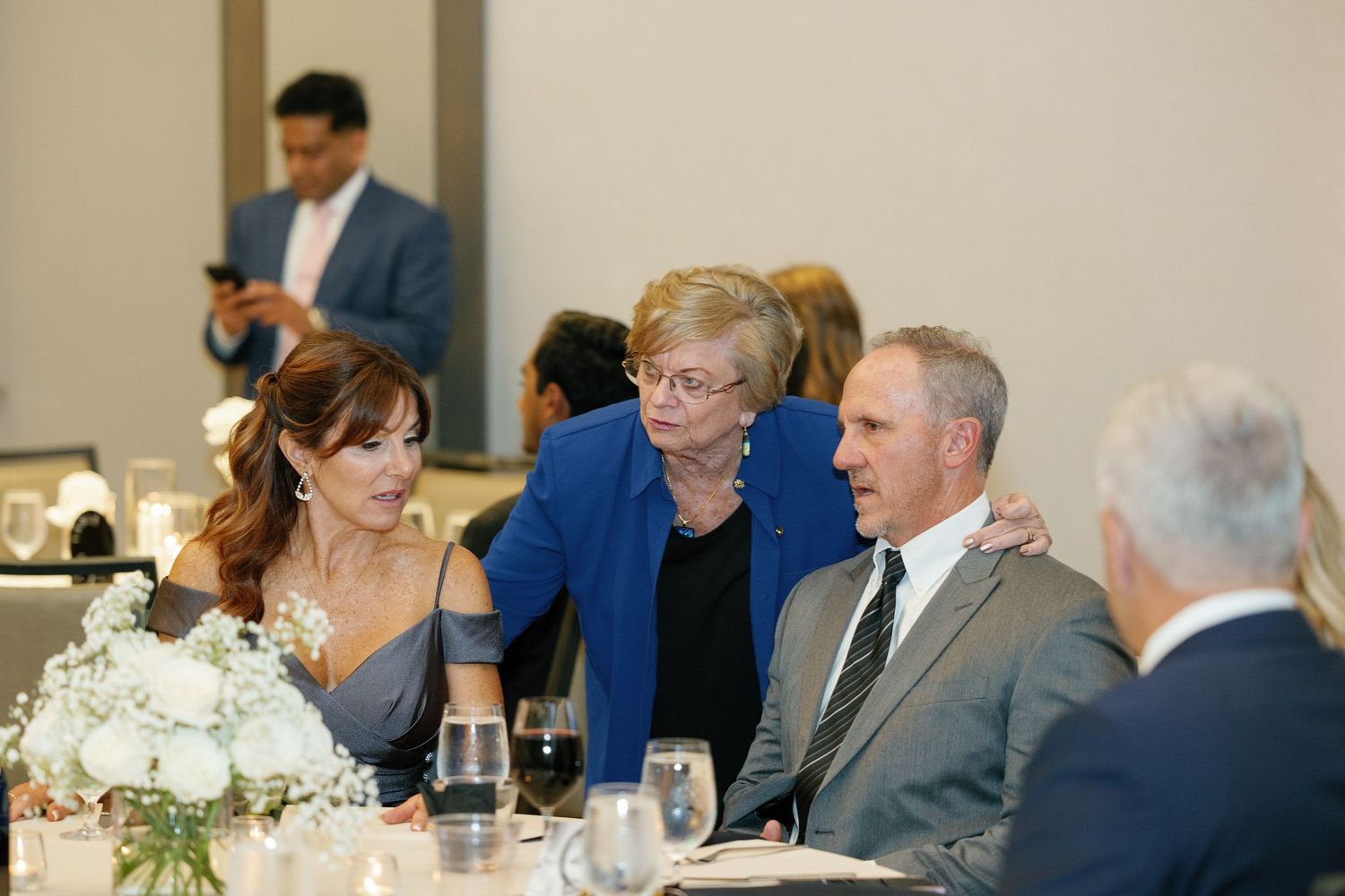 Wedding reception guests seated at elegant tables with white floral centerpieces during dinner service.