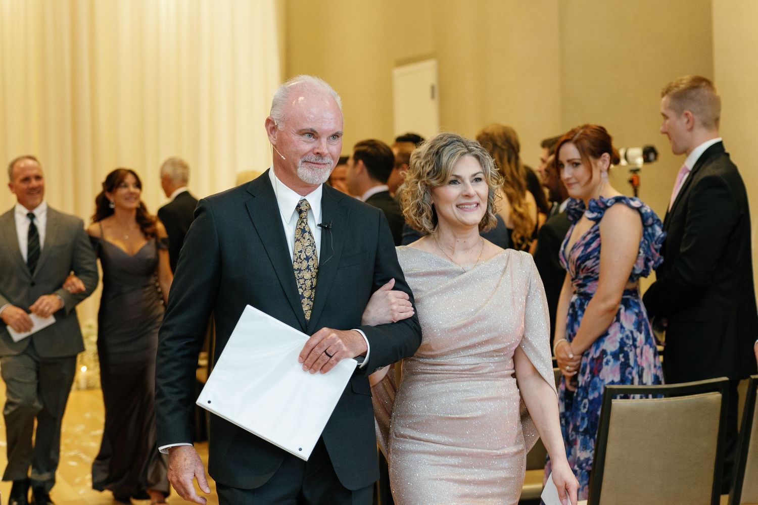 Wedding guests dance and socialize in an elegant ballroom with cream-colored walls during a reception celebration.
