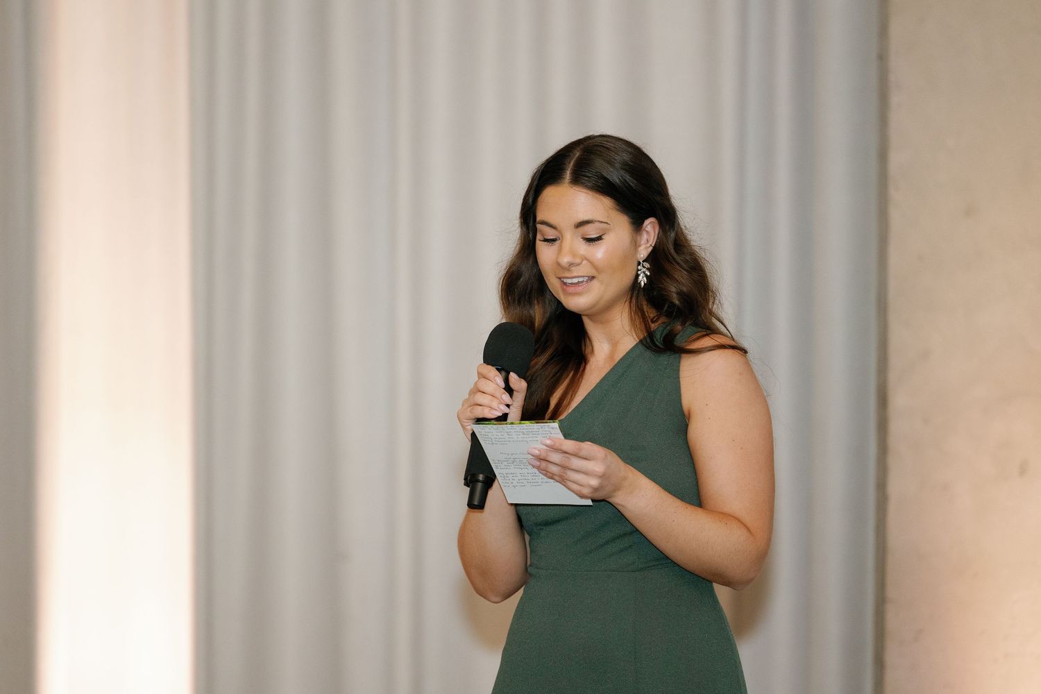 Woman in green sleeveless top takes photos with smartphone while standing in bright interior space.